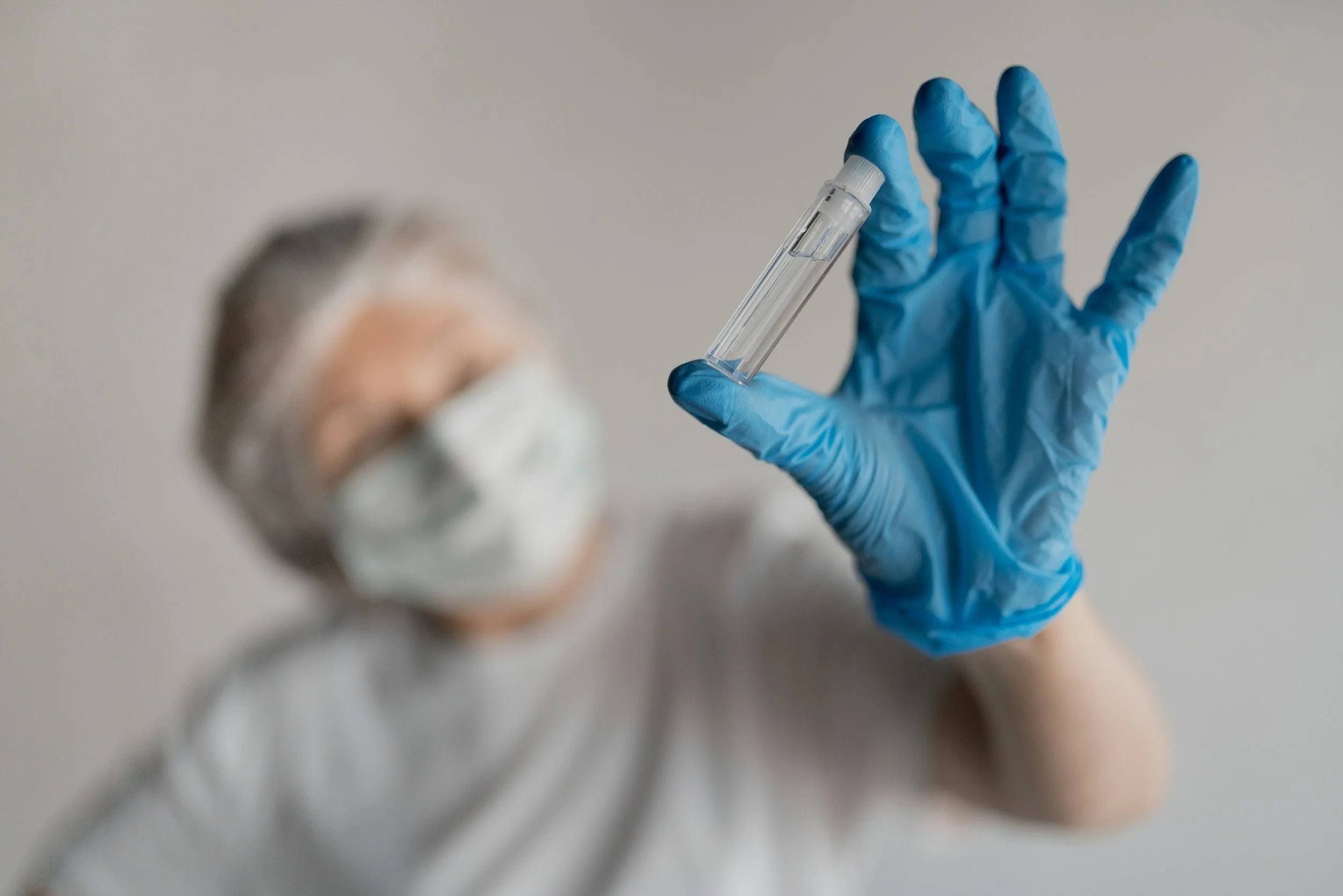 Hand wearing a blue medical glove holding a small clear plastic test tube with a white cap.