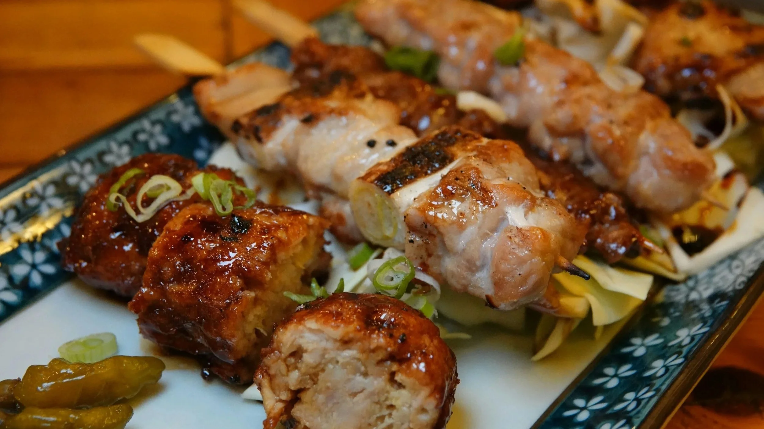 Close-up of skewered grilled chicken and meatballs garnished with chopped green onions on a decorative plate.