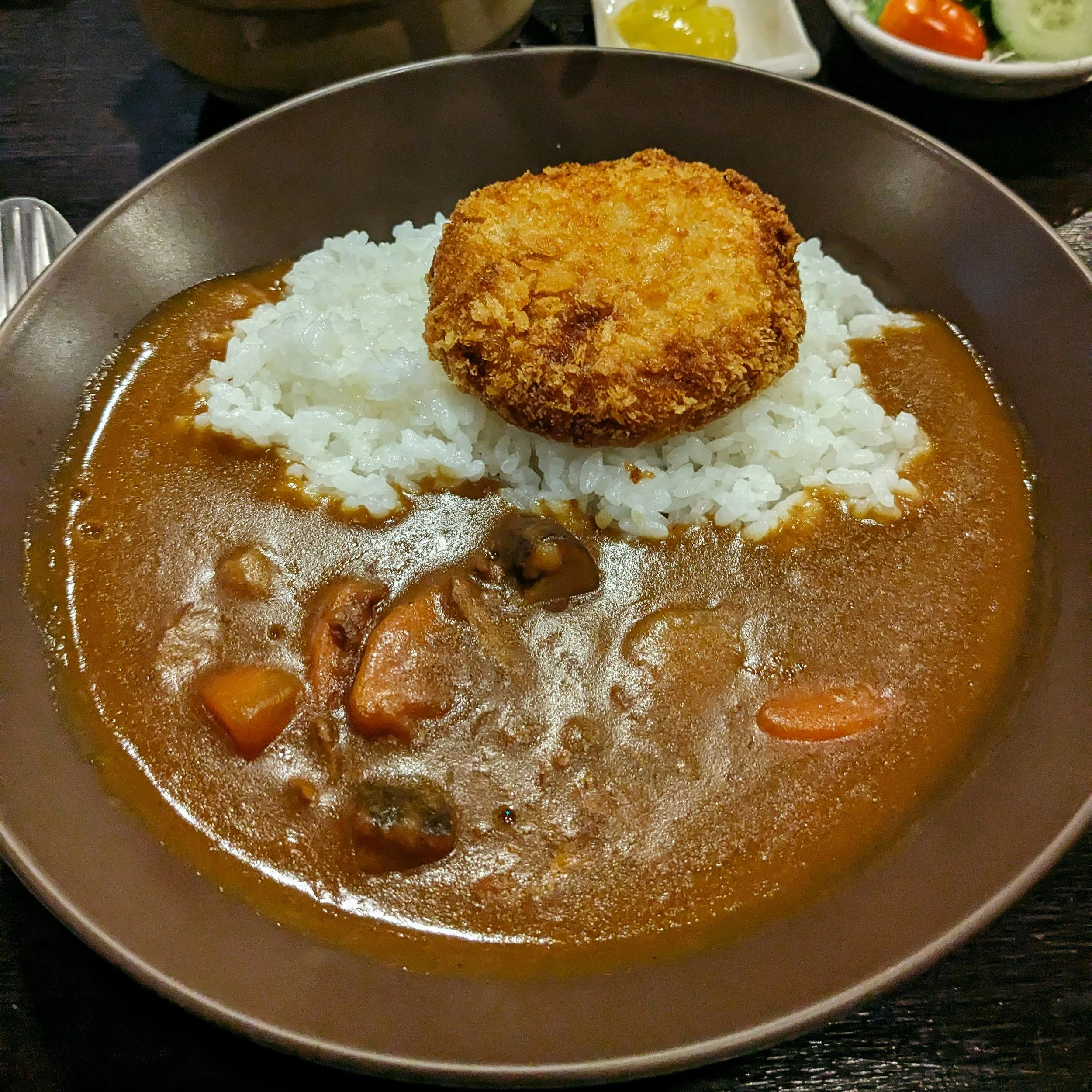 A bowl of Japanese curry rice topped with a deep-fried breaded cutlet, possibly chicken or pork, served with white rice.