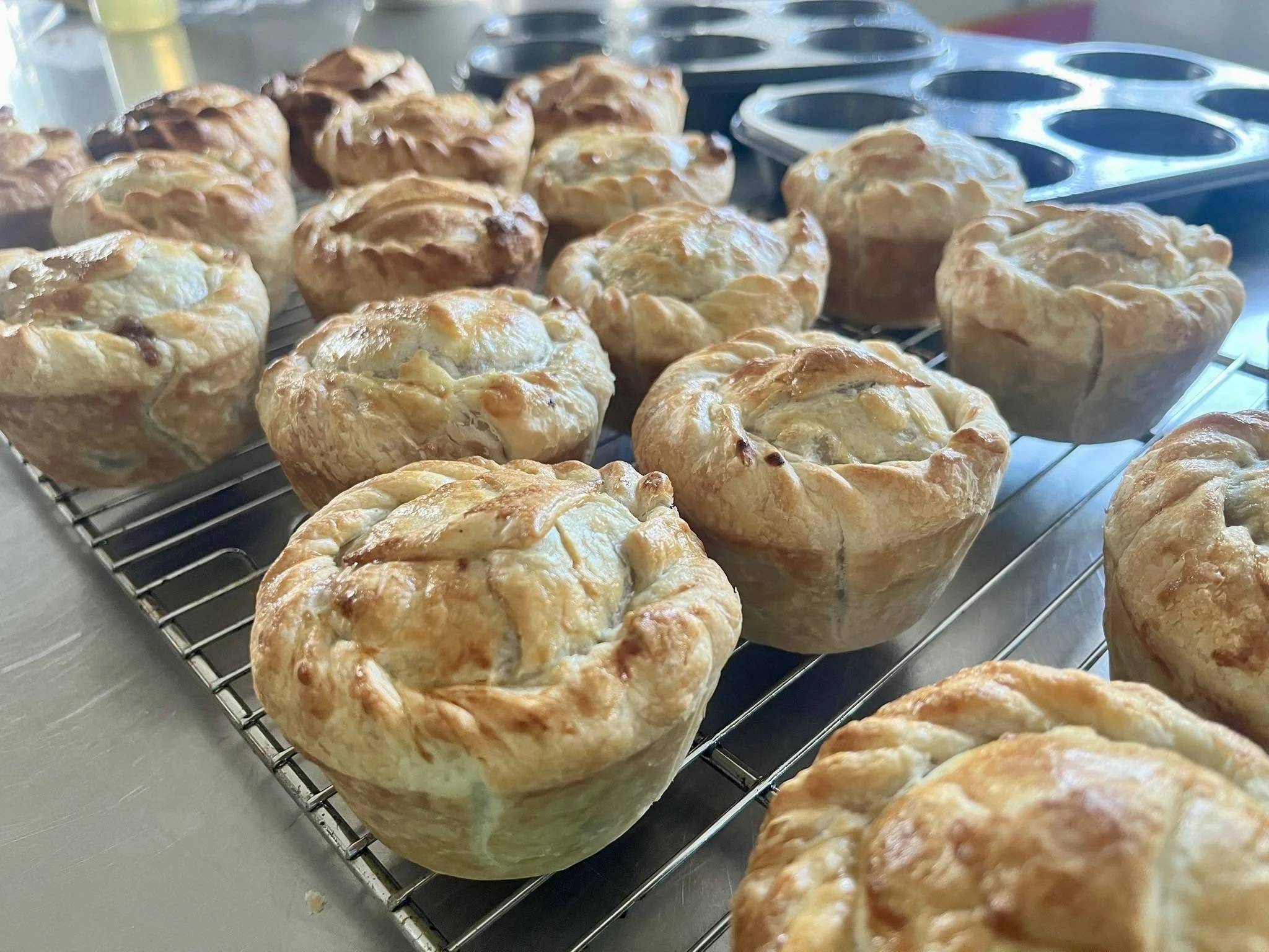 Freshly baked savory pastries with a golden-brown crust cooling on a wire rack in a bakery or kitchen setting
