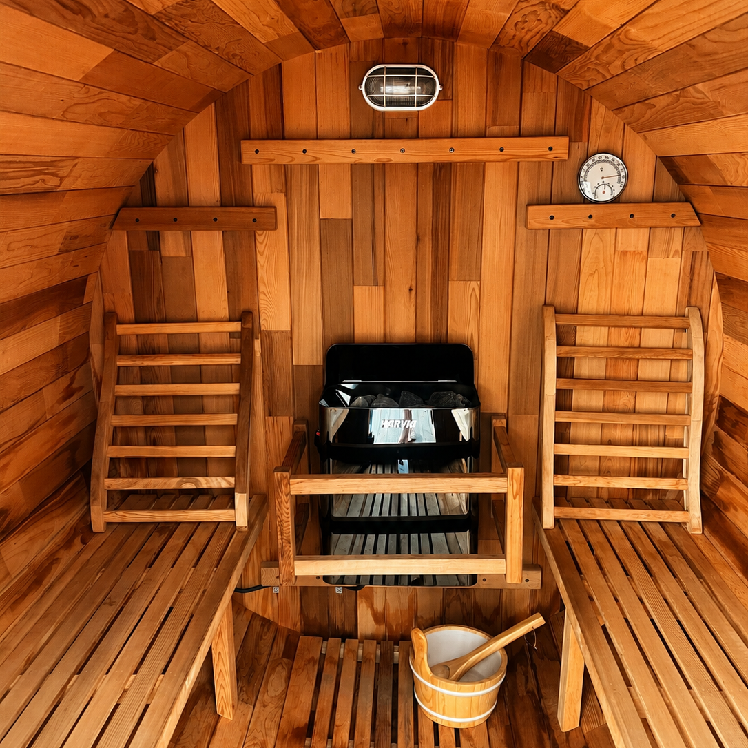 Wood-paneled sauna interior with two wooden benches, a sauna heater, a bucket with a ladle, a thermometer, and a light fixture.