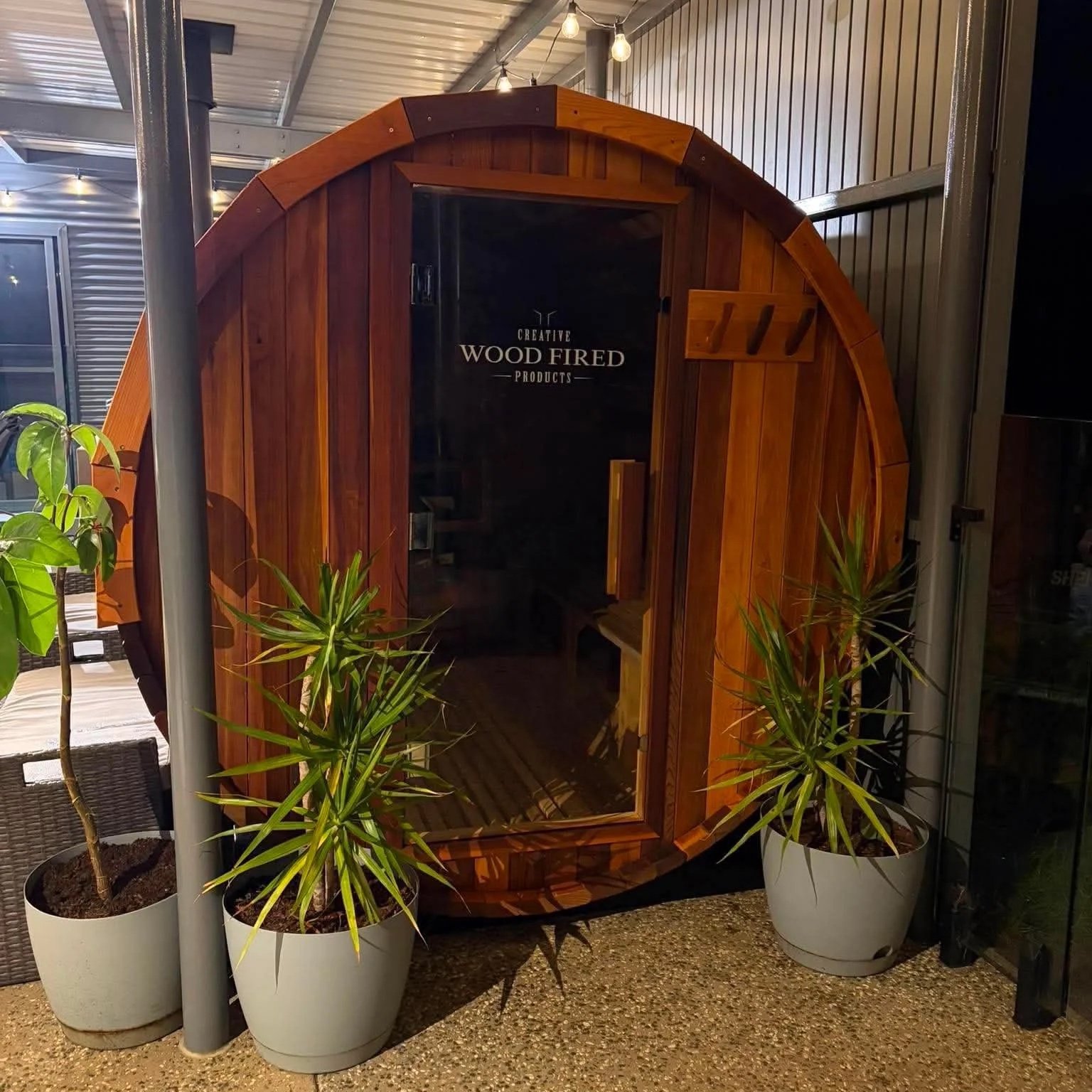 A wooden indoor sauna with sitting bench, surrounded by potted green plants, inside a retail setting.