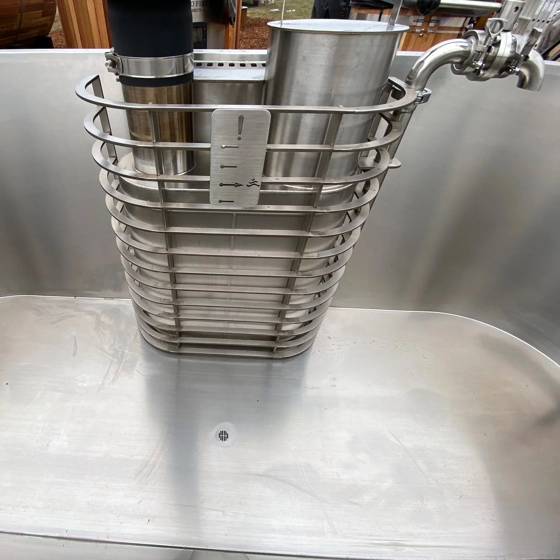 A stainless steel insert with heater chamber for wood fired hot tub. The chamber has a temperature or level marker with an exclamation mark and arrow, indicating fullness.