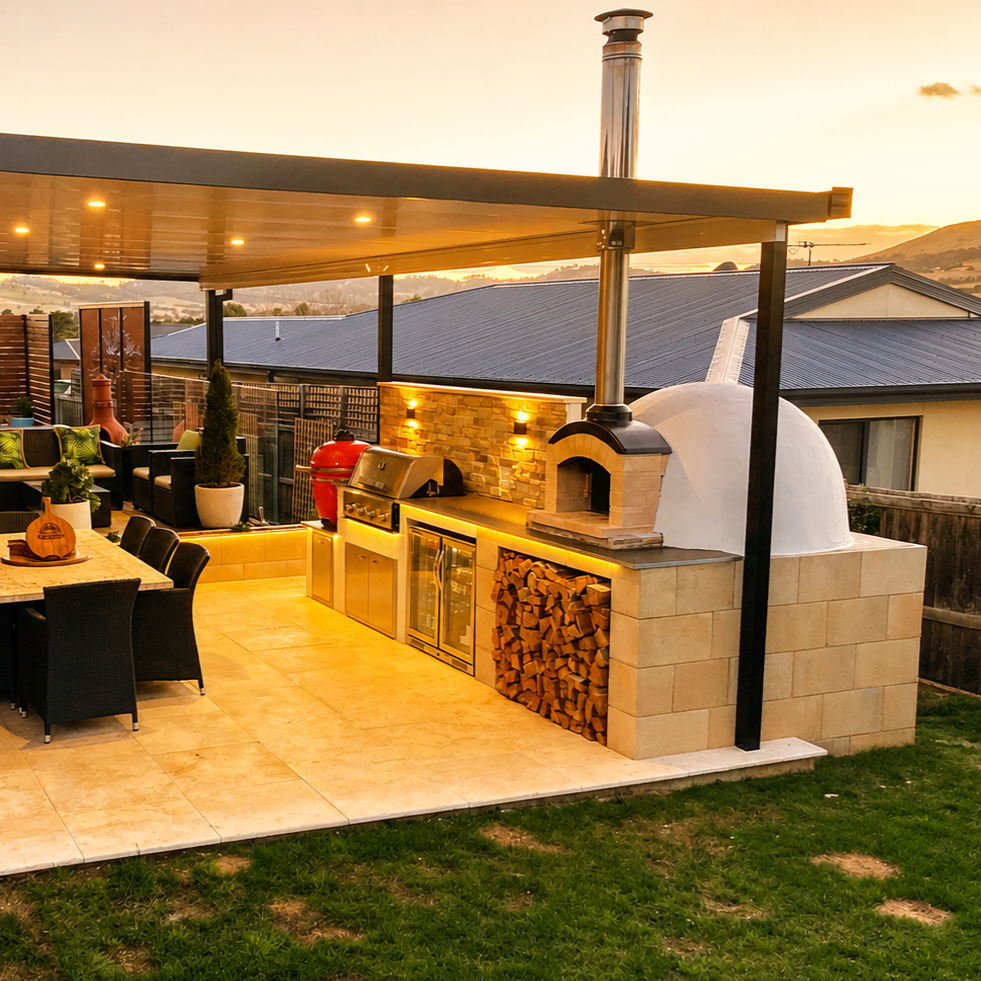 Outdoor kitchen and dining area with a pizza oven, wood storage, refrigerator, and grill, featuring a covered patio, seating, potted plants, and a sunset view.