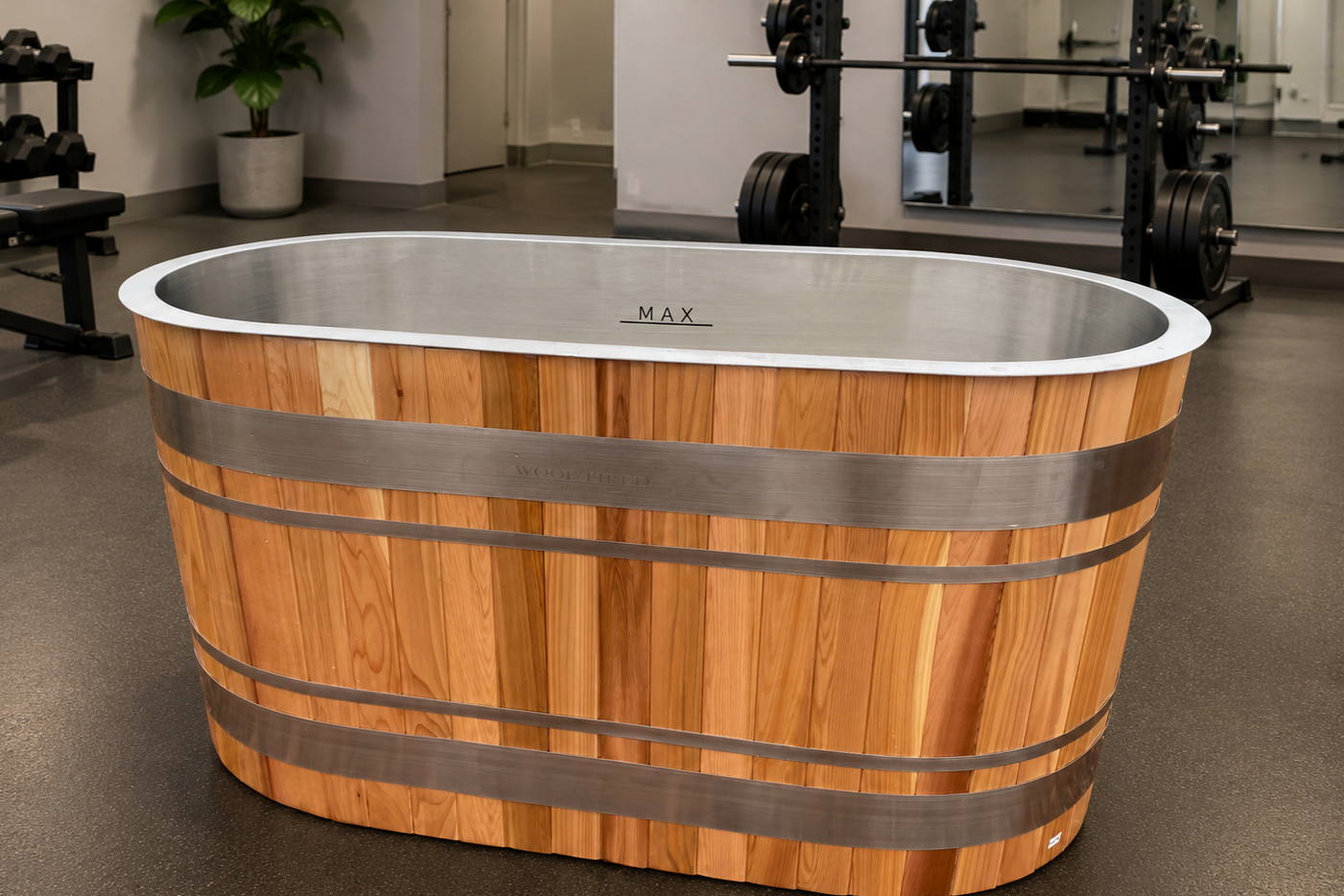 A cedar timber ice bath with a metal rim and metal bands, located in a gym or fitness center.