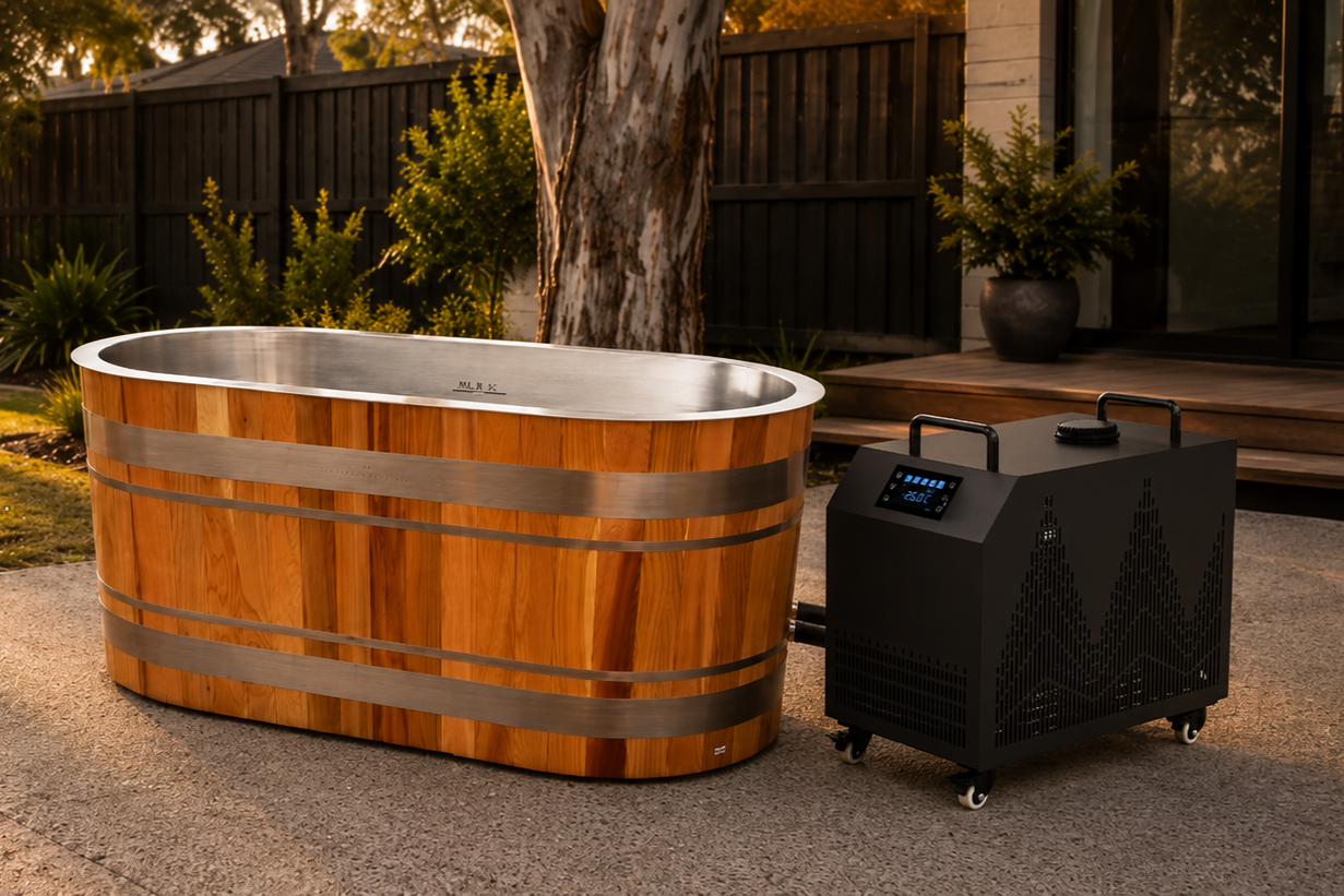 A wooden ice bath connected to a black portable ice bath or chiller unit with a digital display, set on a concrete patio with trees, plants, and a fence in the background.