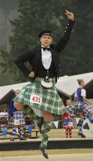 Man dressed in traditional Scottish Highland dress, including a tartan kilt, sporran, and knee-high socks, participating in a highland dance competition.