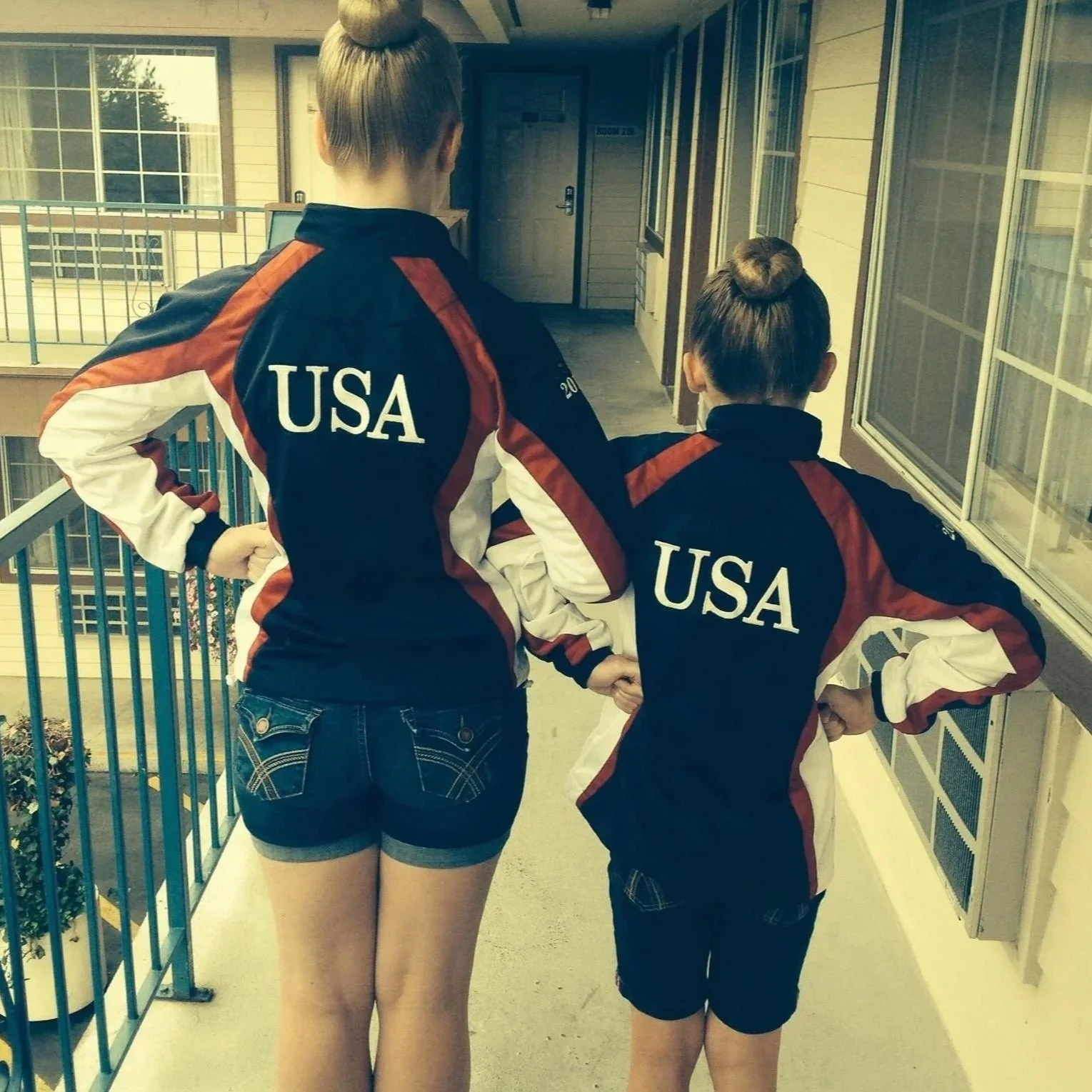Two girls wearing USA dance jackets standing in first position facing back.