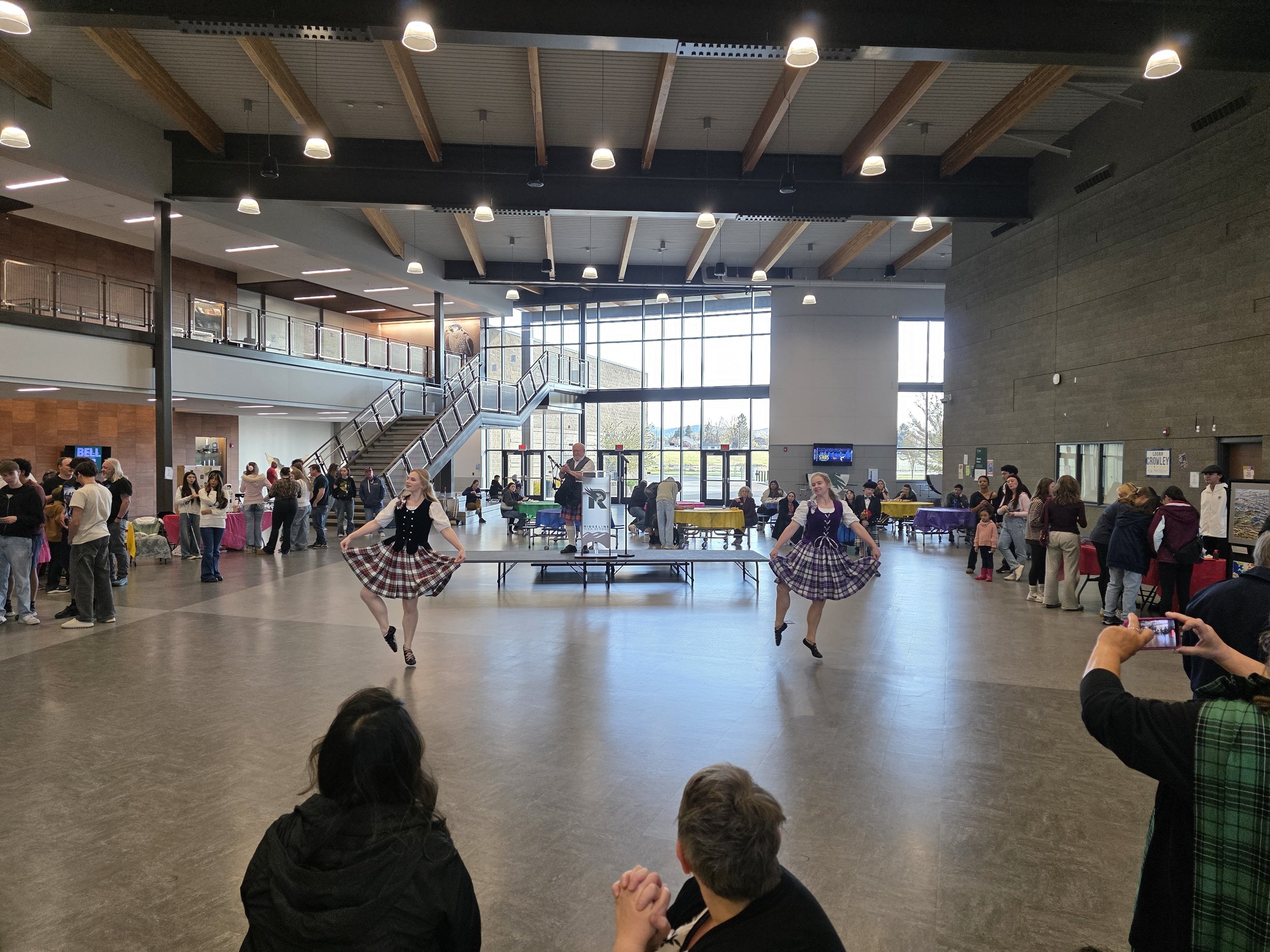People gathered in a high school watching a performance of traditional Scottish Highland Dancing with traditional Scottish Bagpipes.