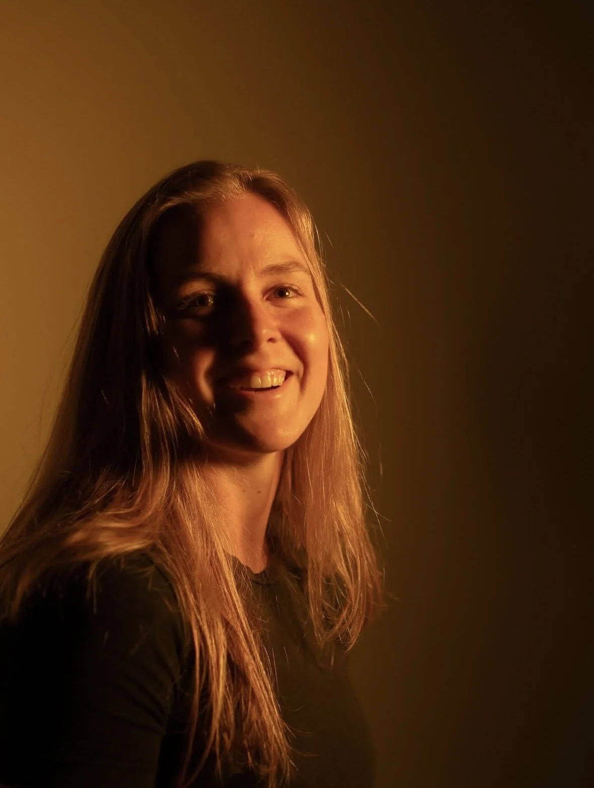 A woman with long wavy red hair smiling in warm, dim lighting.