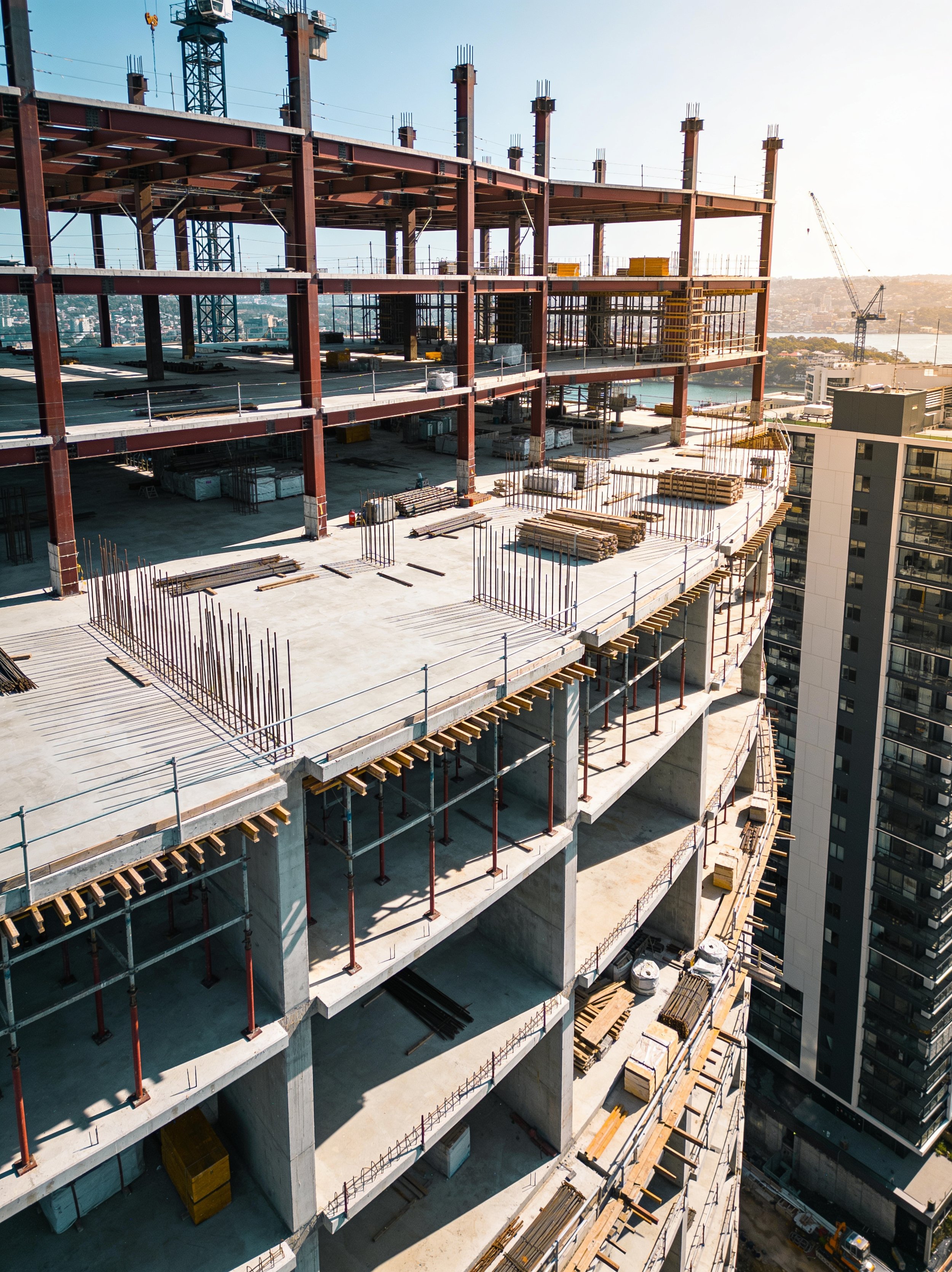 Construction site of a high-rise building with multiple floors under construction, with steel beams, concrete slabs, and construction materials visible.