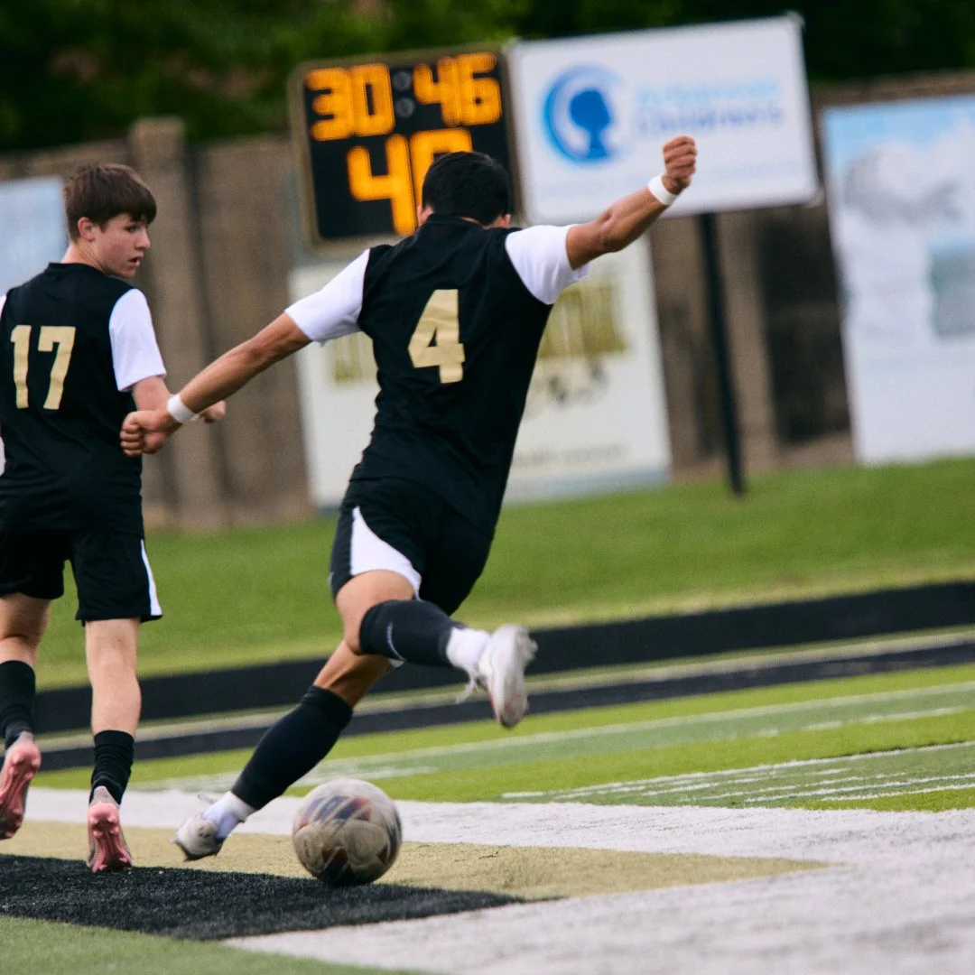 Two young soccer players in black jerseys with numbers 17 and 4, chasing a soccer ball on the field, with a scoreboard in the background showing 30:45.
