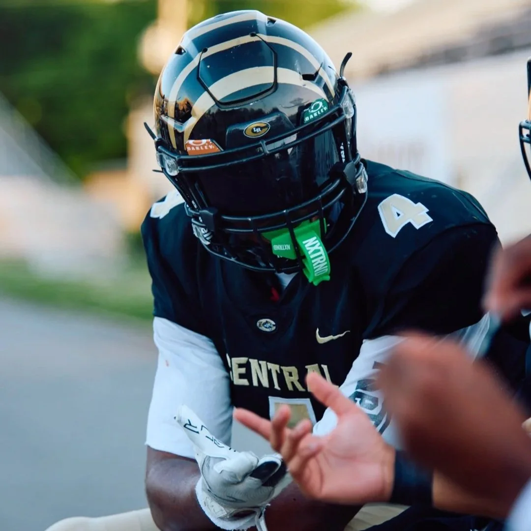 A football player wearing a black and white helmet and black jersey with the number 4, sitting on the sidelines during a game.