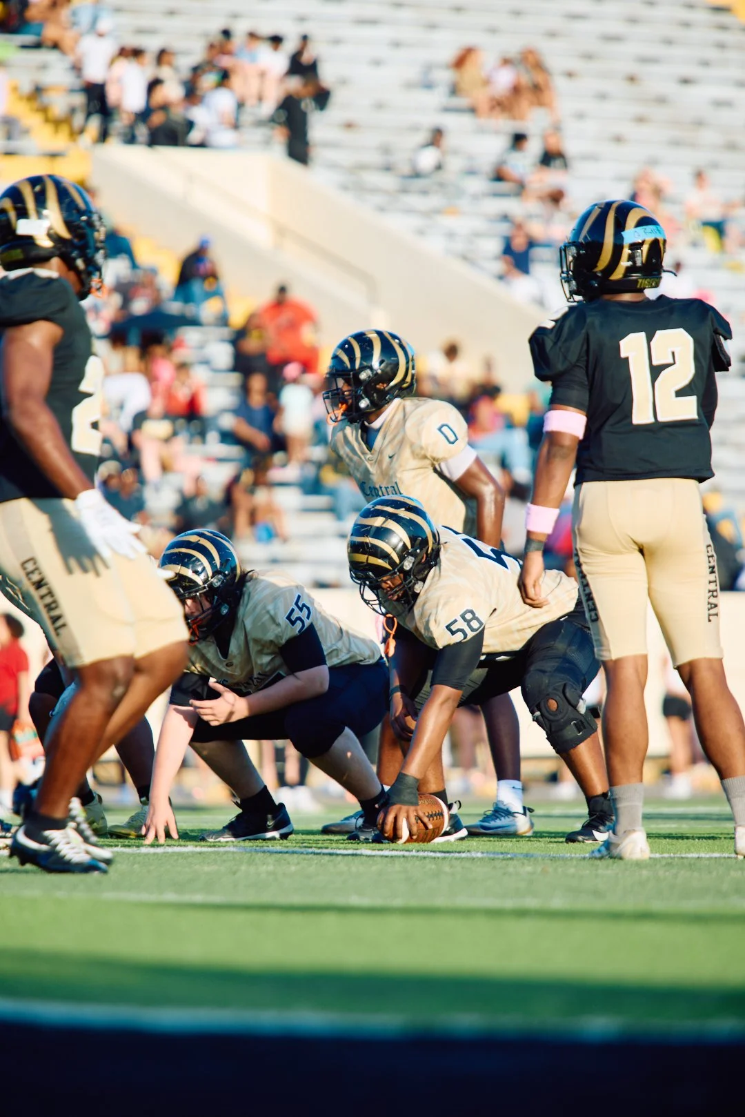American football players on the field with helmets and uniforms, preparing for a play during a game in a stadium with spectators in the background.