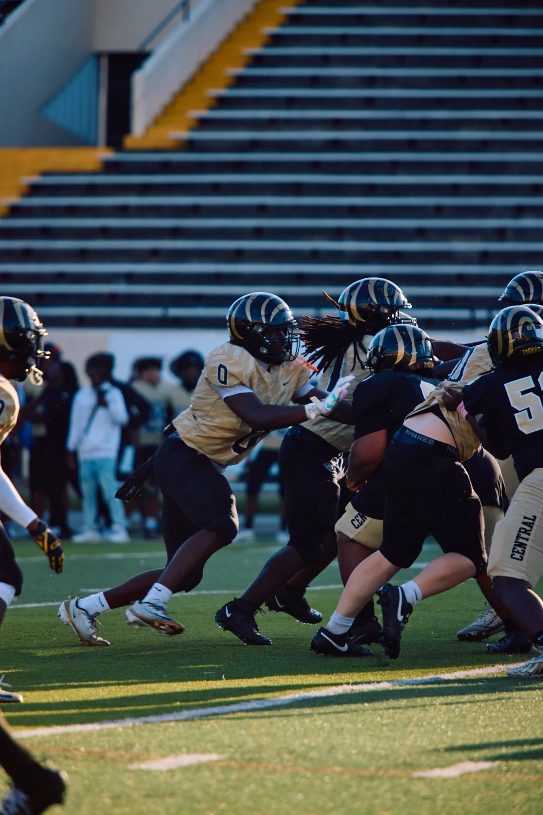American football players in black and gold uniforms during a game on the field with spectators in the background.