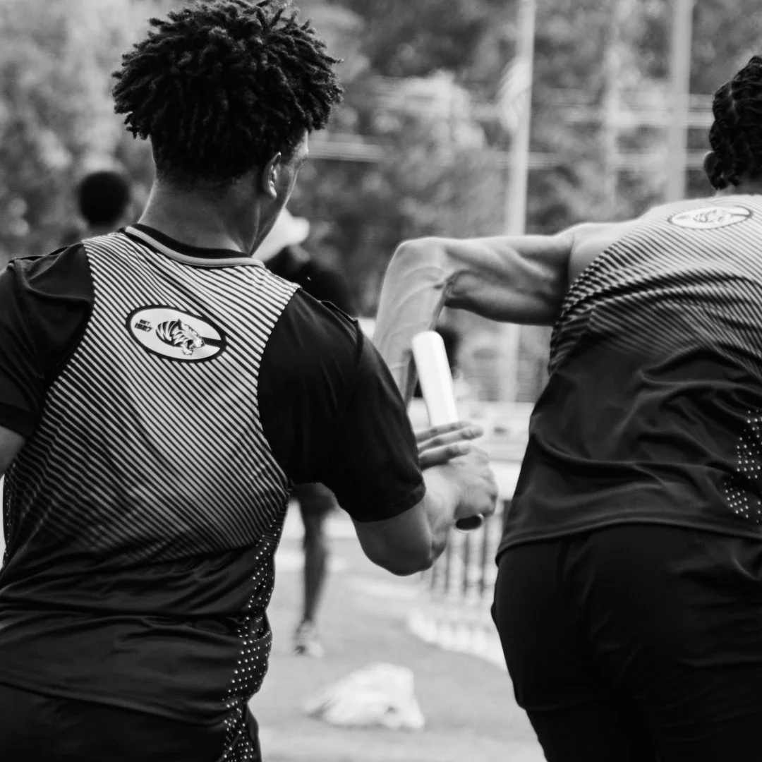 Two athletes in athletic gear passing a relay baton during a race.