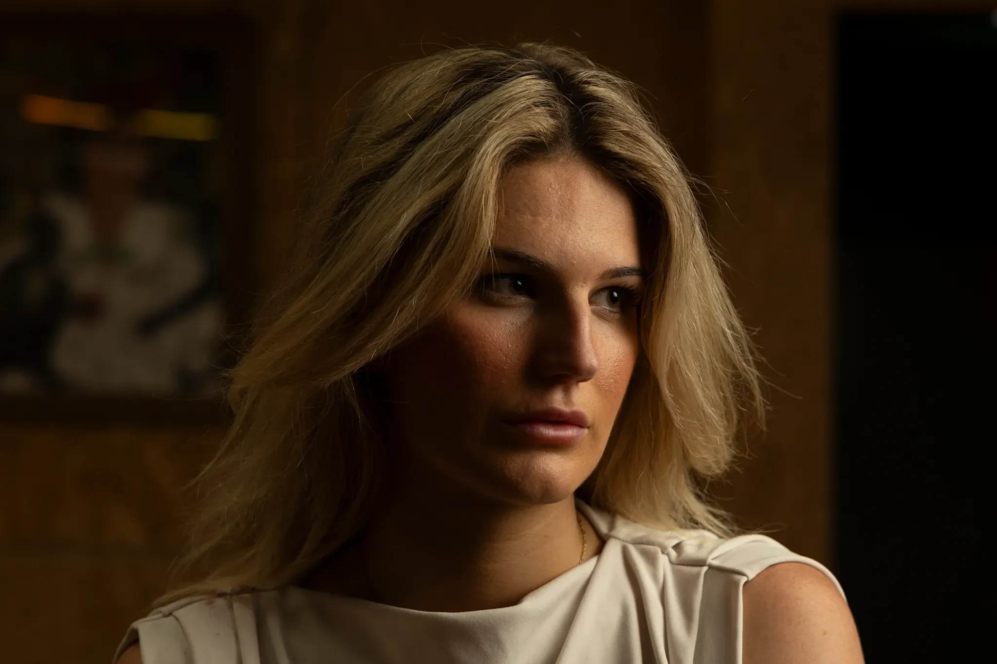 Close-up of a woman with blonde hair, looking to the side, wearing a white dress or top.