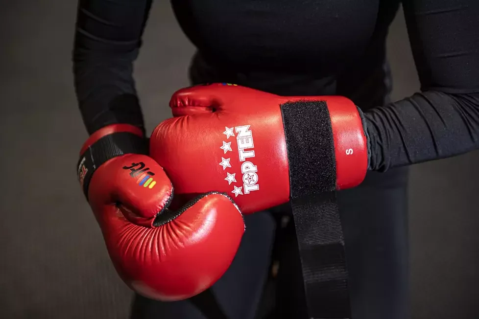 A person wearing red boxing gloves with the brand name 'TOKTEN'. The gloves are secured with a black strap. The person is dressed in a black long-sleeve shirt.