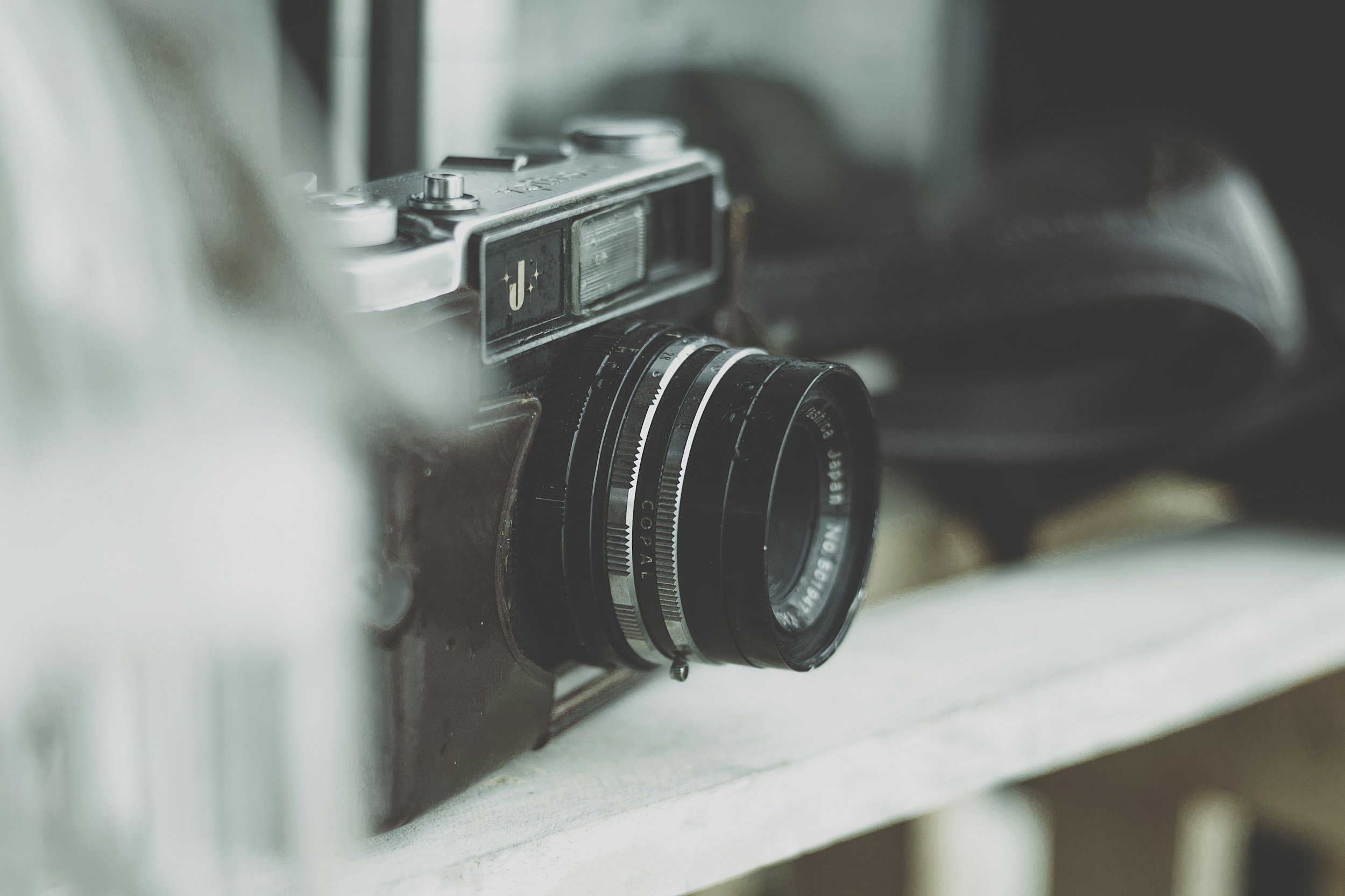Close-up of a vintage camera with a black and silver design resting on a white surface.