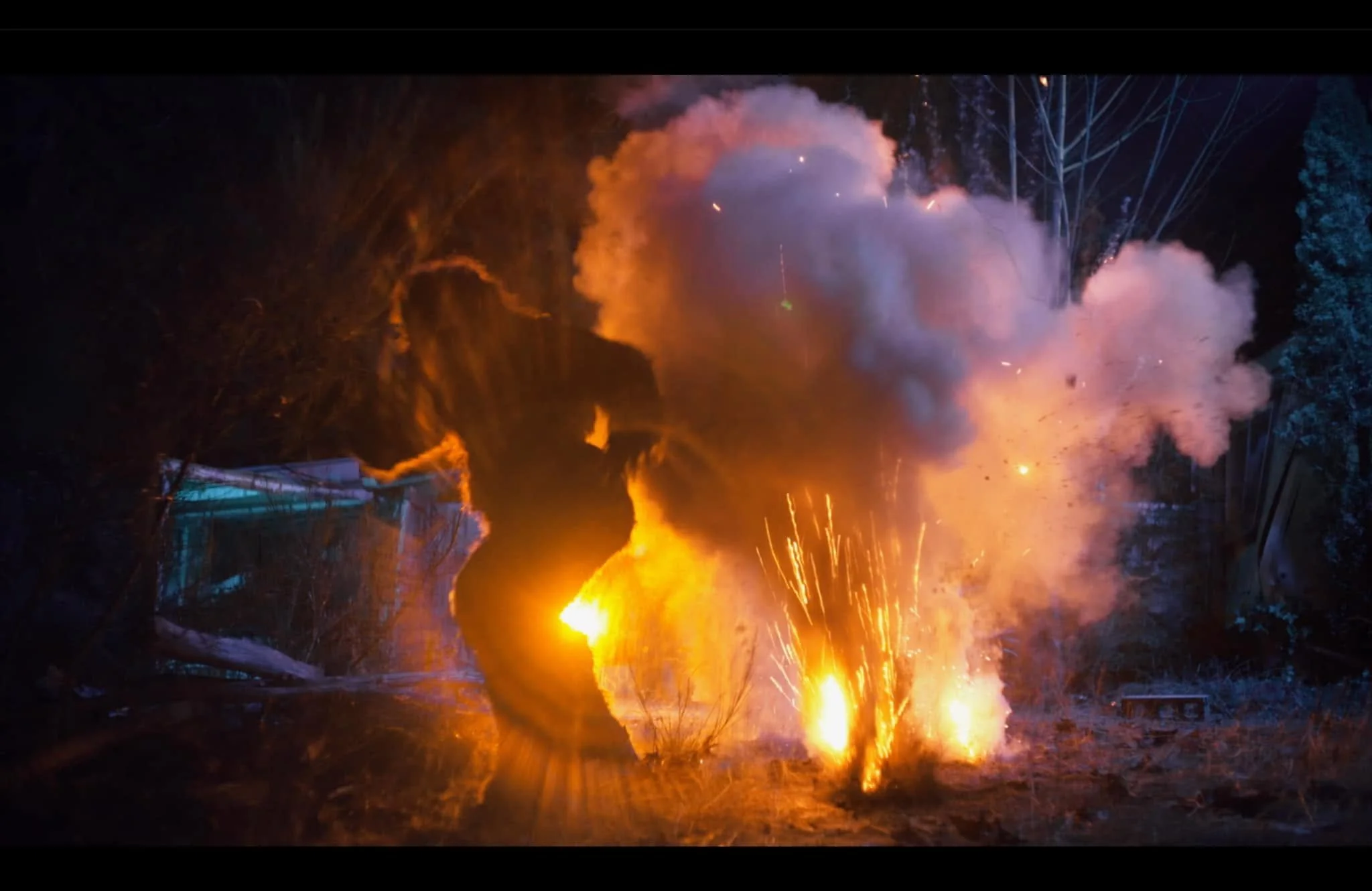 Fireworks explosion with orange, purple, and white smoke and sparks in a wooded outdoor area at night with a werewolf running away.