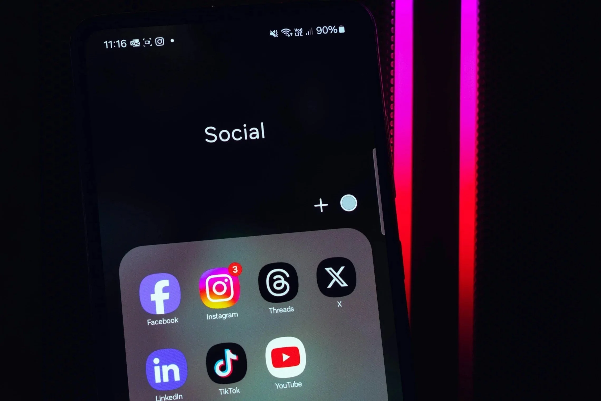 A smartphone screen displaying a social media folder with icons for Facebook, Instagram, Threads, X, LinkedIn, TikTok, and YouTube.