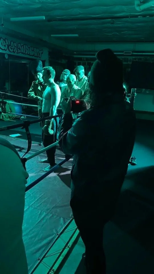 Tyler Darkow filming group of undead people watching a boxer in a boxing ring under blue lighting.