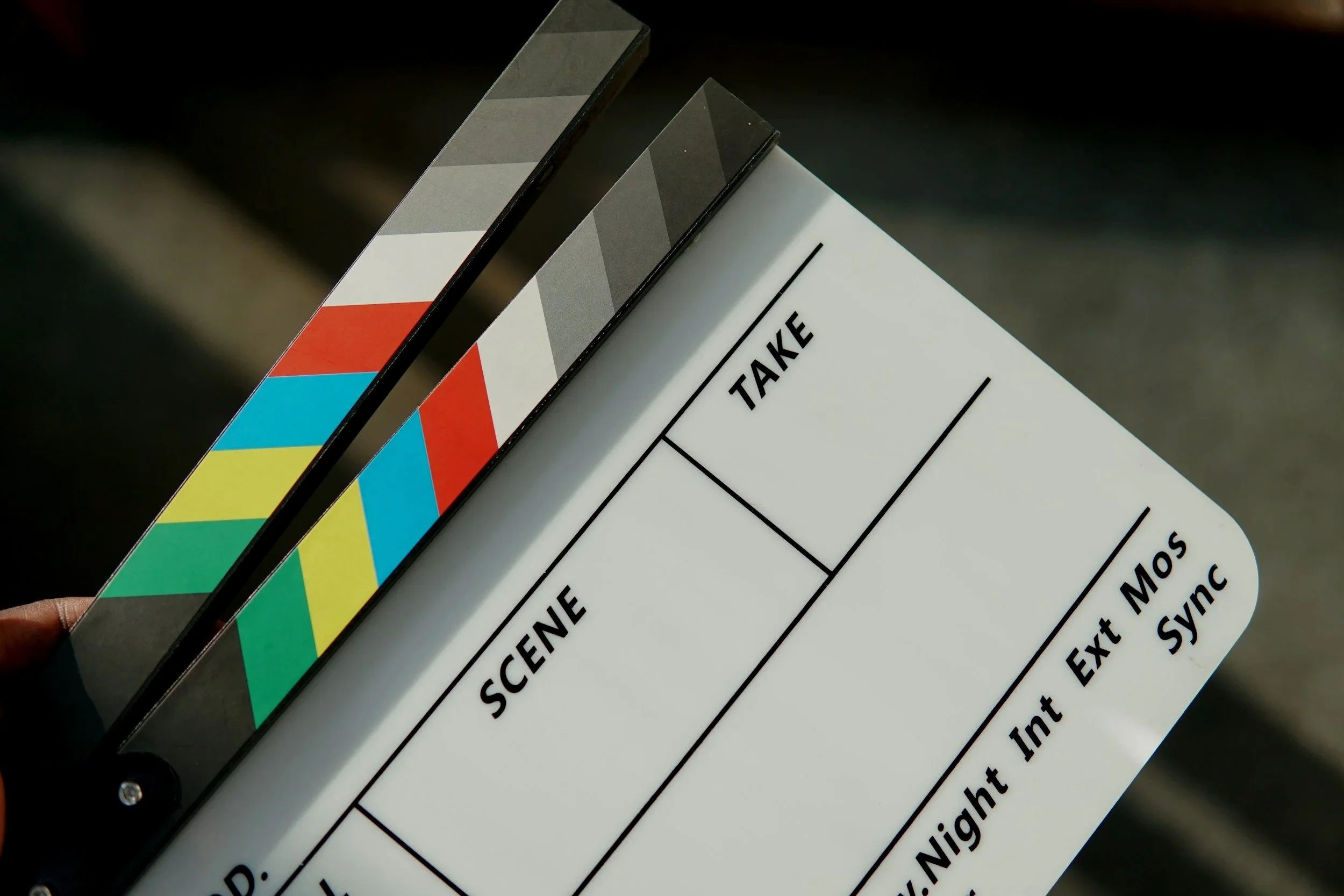 A close-up image of a film clapboard or clapperboard used in filmmaking, with colorful stripes on the top edge.