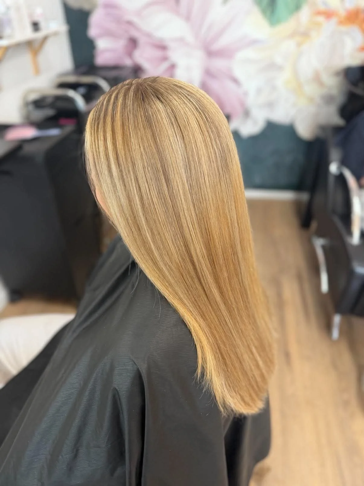 Woman with long, straight, shiny blonde hair in a salon setting, wearing a black cape.
