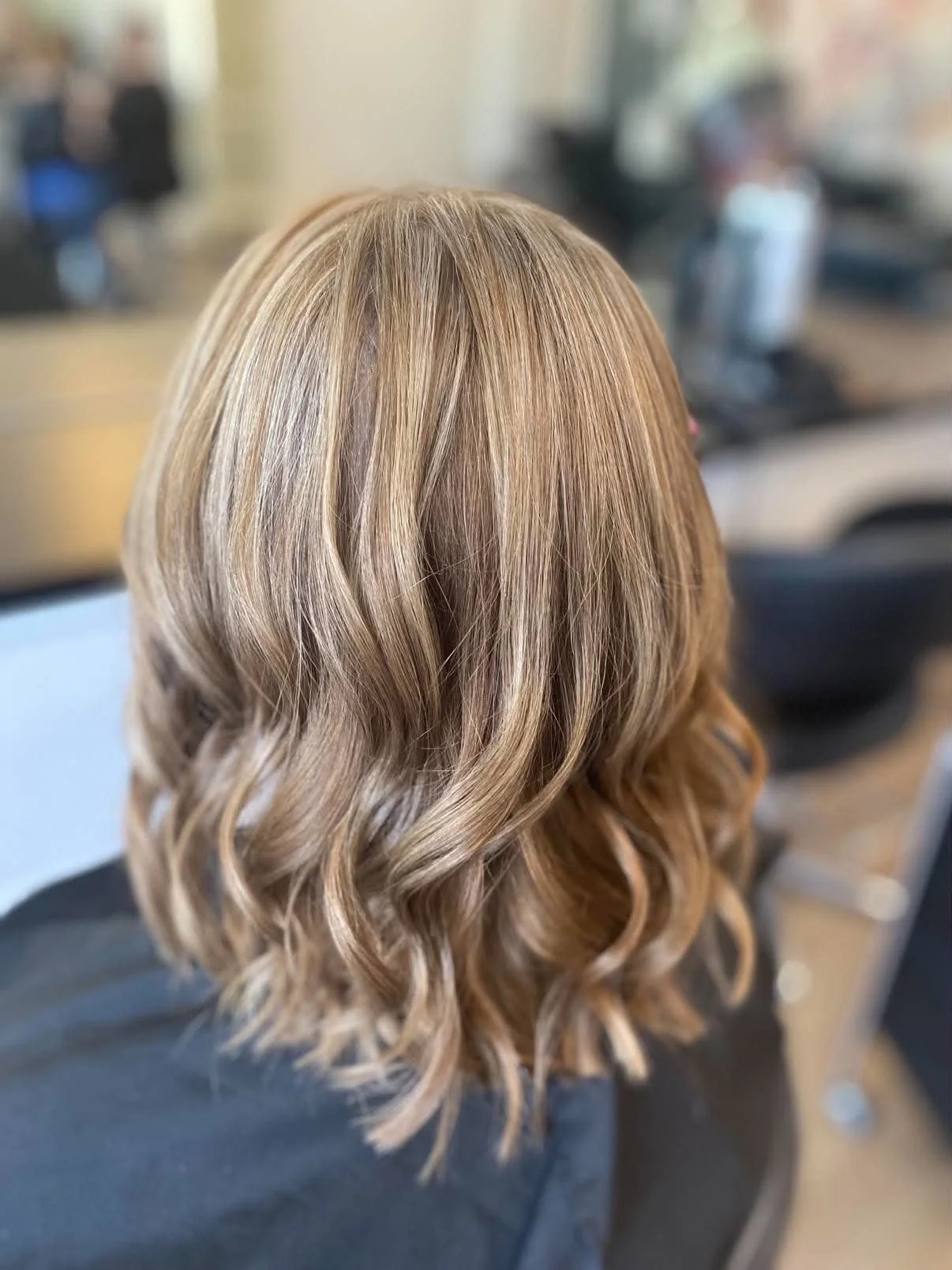 Woman with shoulder-length, wavy blonde hair in a salon setting.