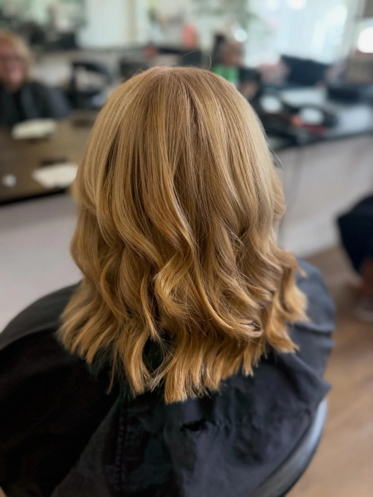 Back of a woman's head showing wavy blonde hair, sitting in a salon or similar setting.