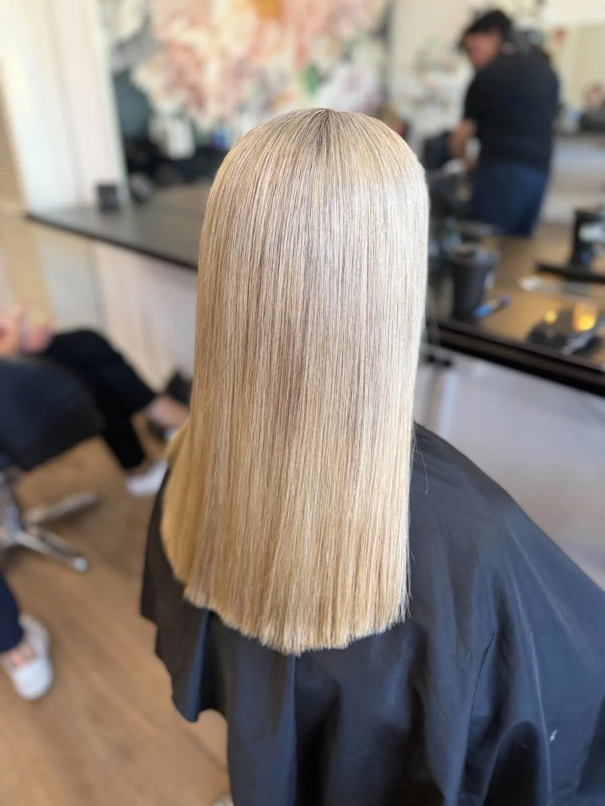 Back view of a person with long, straight, blonde hair in a hair salon.