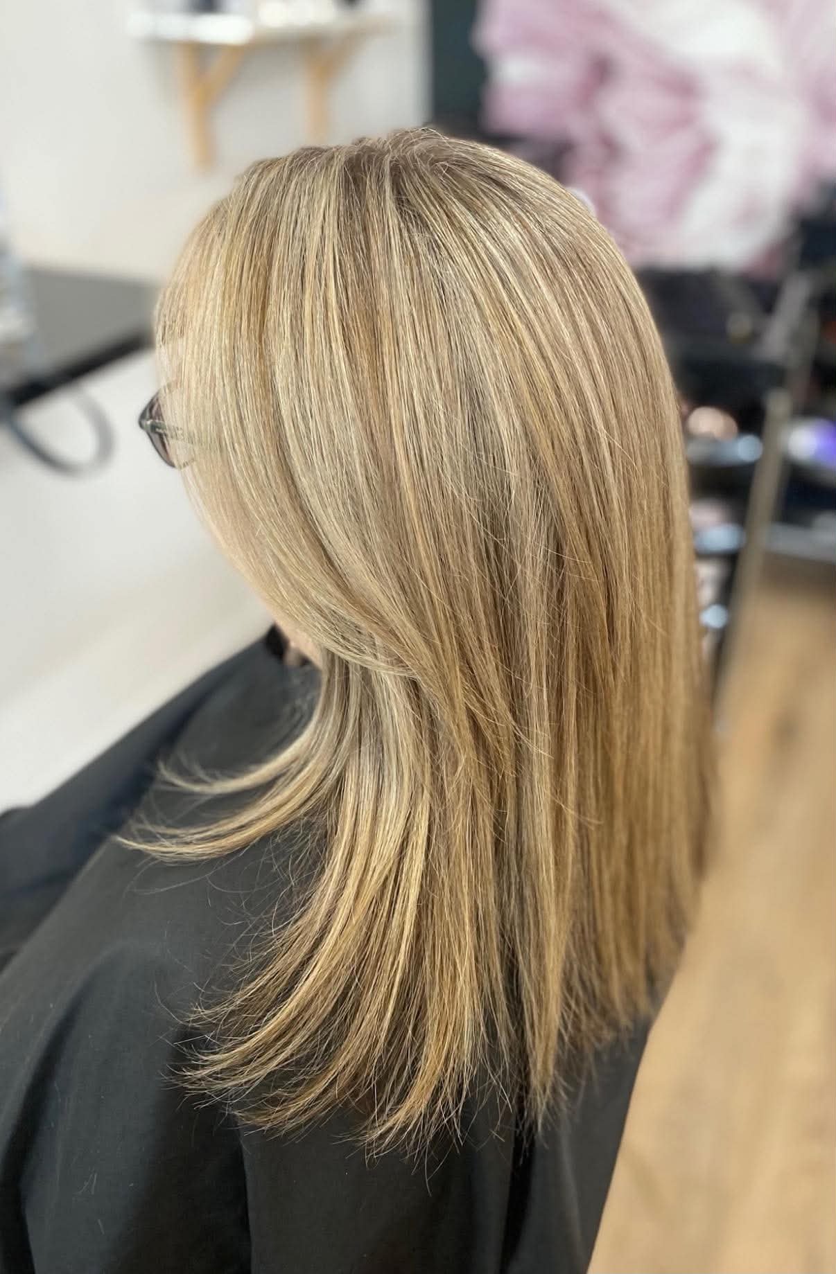 Woman with long, blonde, straight hair seated in a salon chair, with hair styled and separated, in a salon setting.