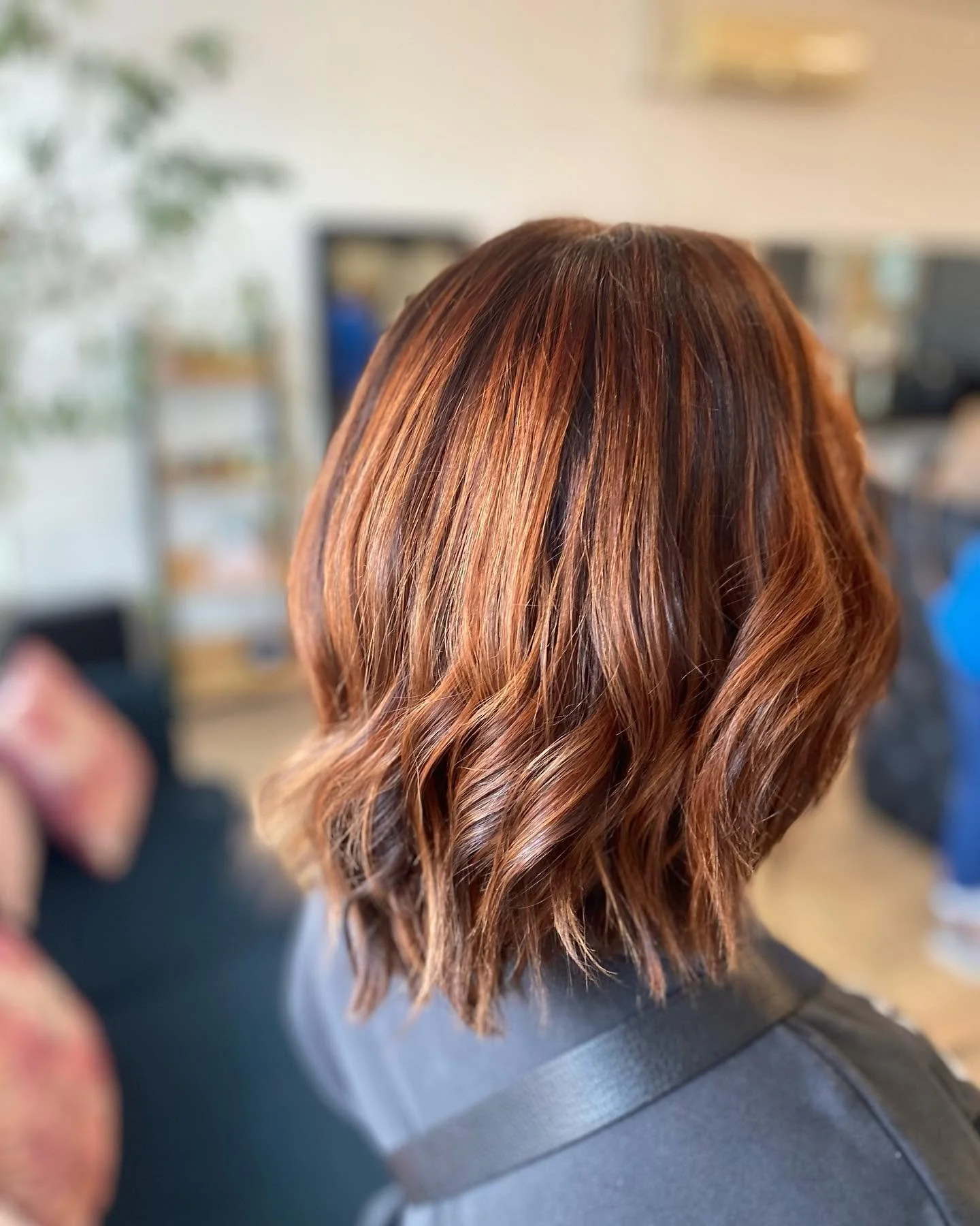 Back of a person's head with shoulder-length, wavy, reddish-brown hair in a salon setting.