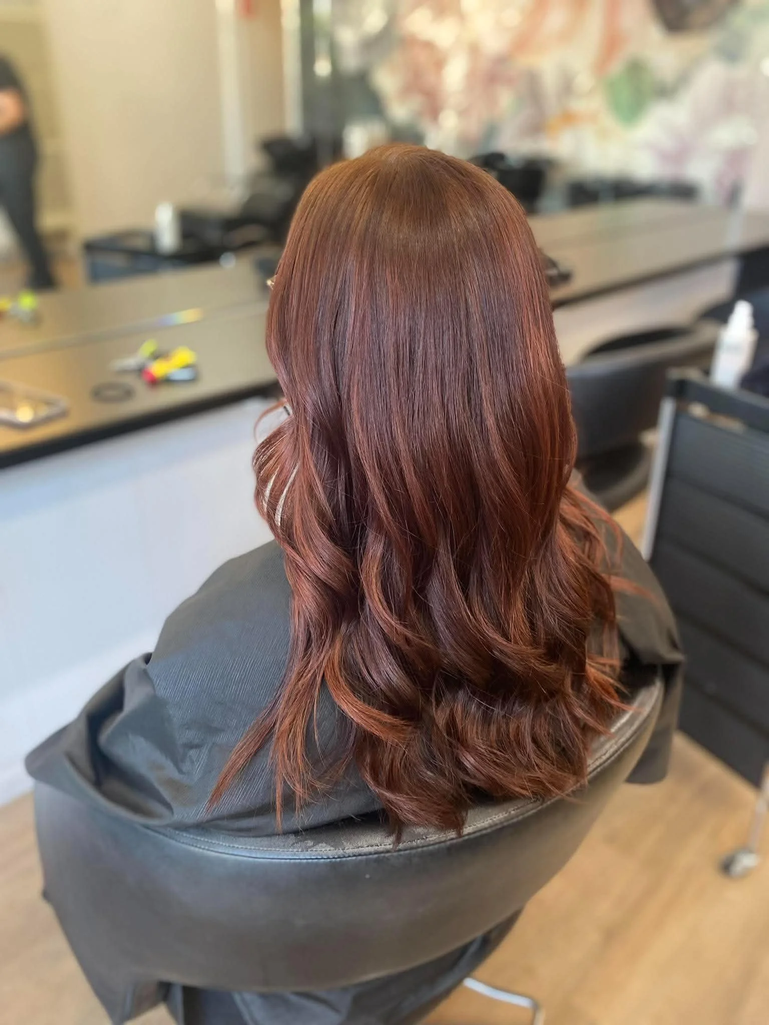 Back view of a person with long, wavy, auburn hair sitting in a salon chair.