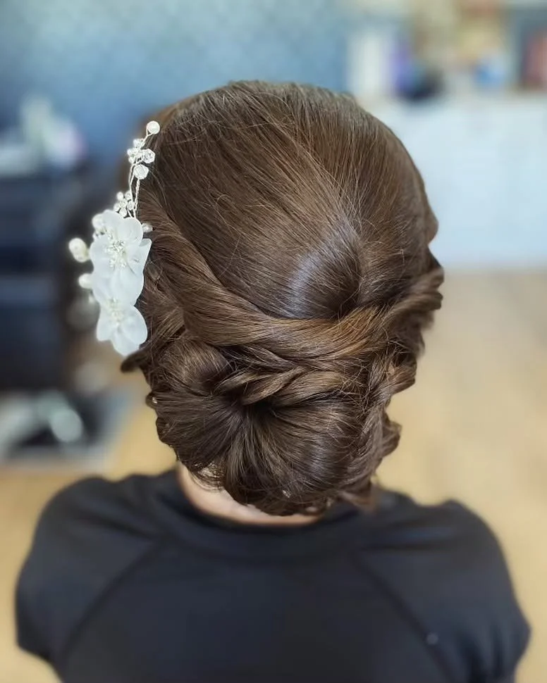 Elegant brunette hairstyle with a floral hairpiece, styled in a vintage updo.