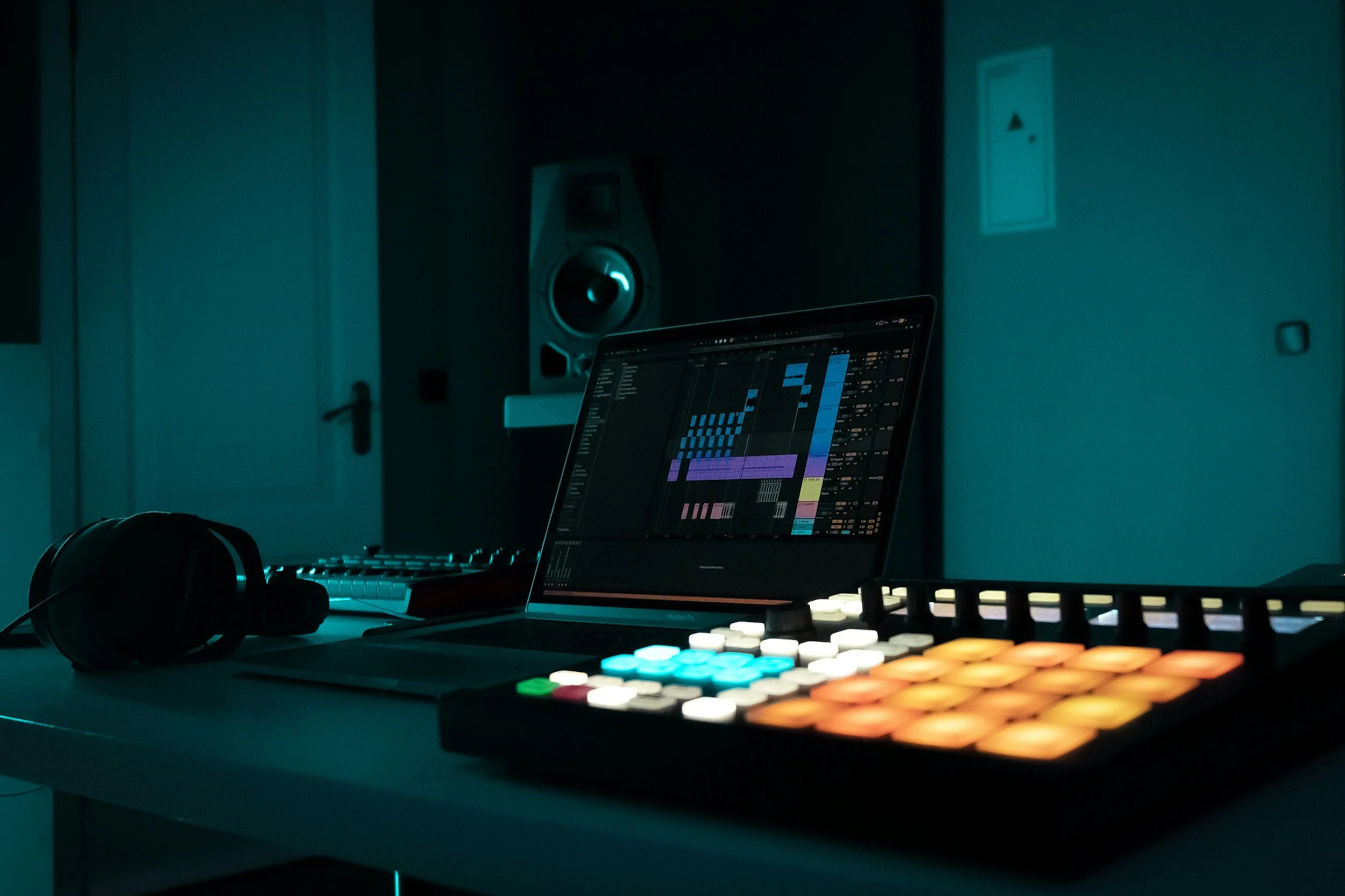 A music production workspace with a laptop displaying digital audio workstations, a colorful MIDI controller, a pair of black headphones, and a studio monitor at Brisbane music studio, Air Audio.