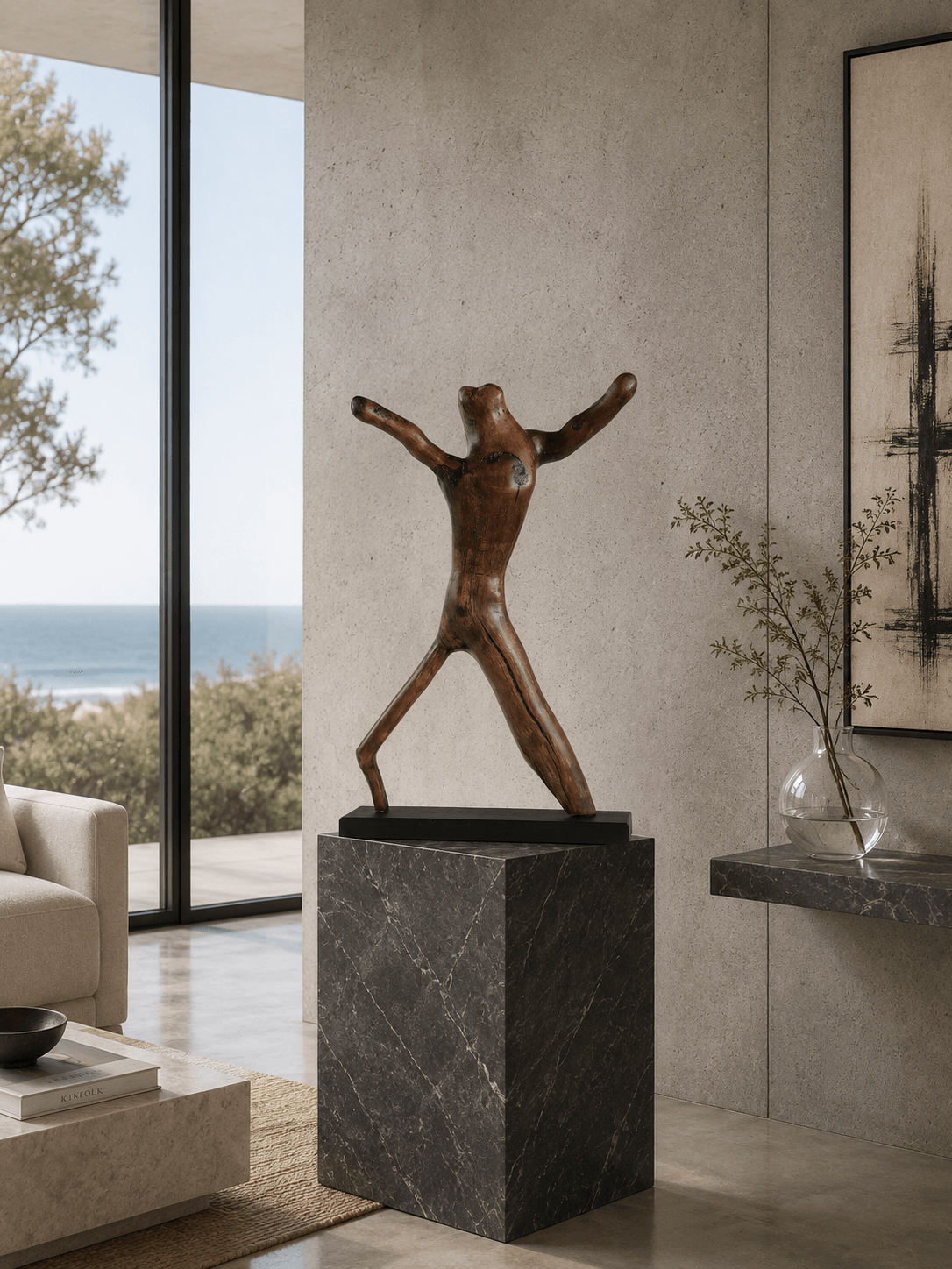 The abstract wood sculpture Alien Dancer, displayed on a tall dark grey marble plinth in a contemporary coastal home with ocean views and a minimalist design.