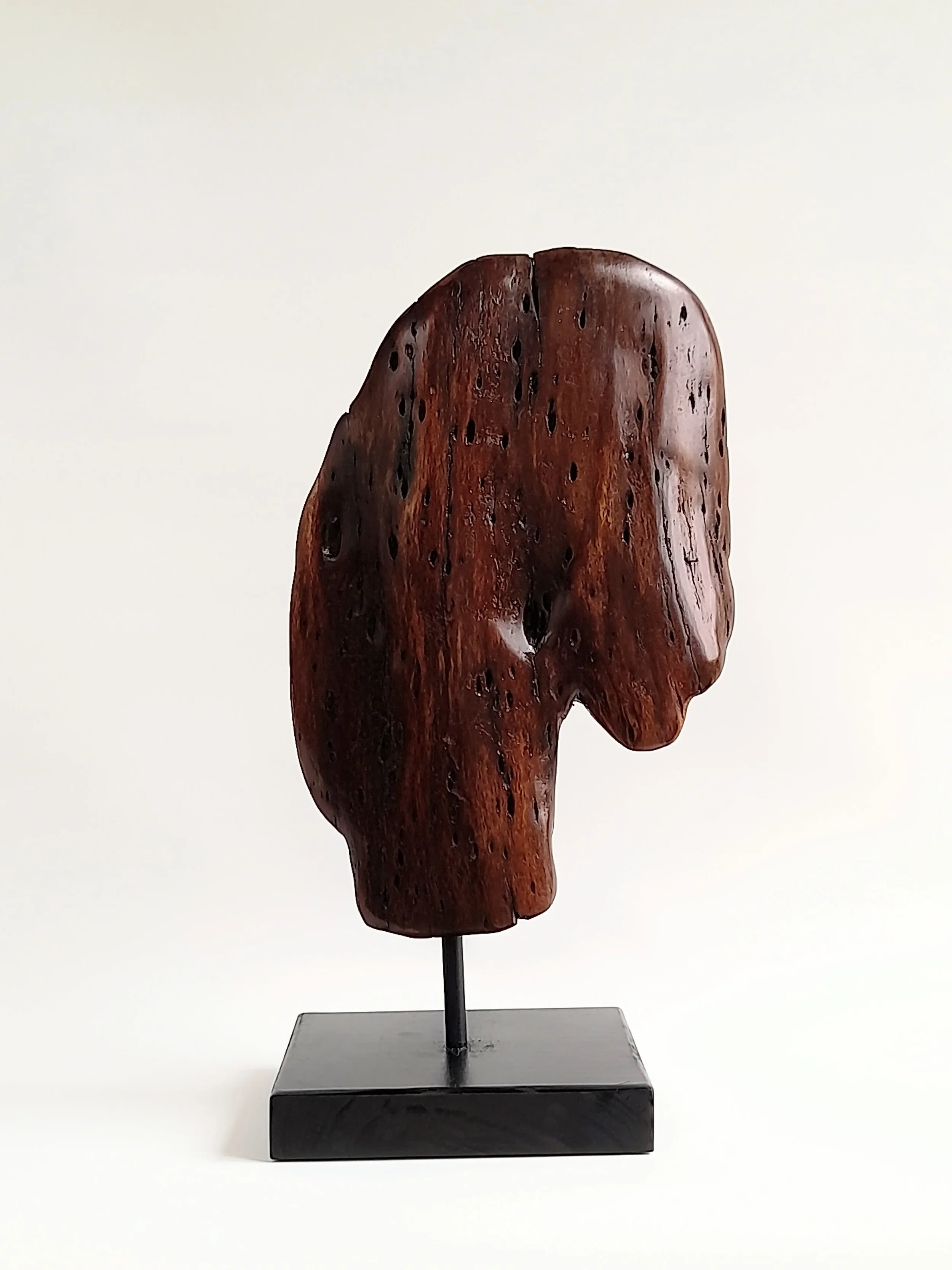 Dual-sided hand-carved dark Brushbox wood head sculpture with natural weathered details on a black stand titled Weathered Soul.