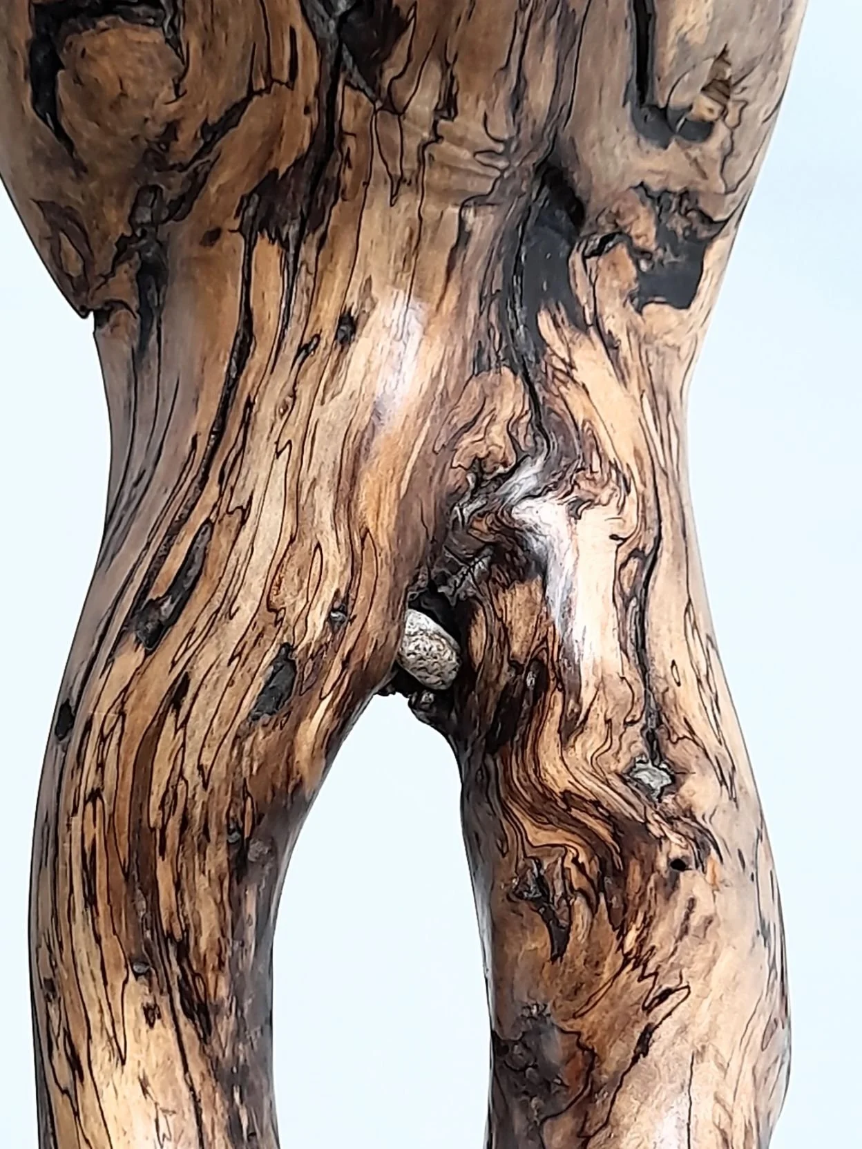 Close-up detail of Still Standing sculpture showing chiselled timber textures, organic grain patterns, and natural-fitted river stone element.