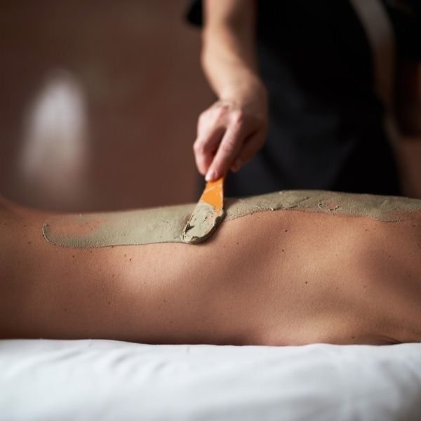 Person applying clay mixture to a person's back with a spatula.