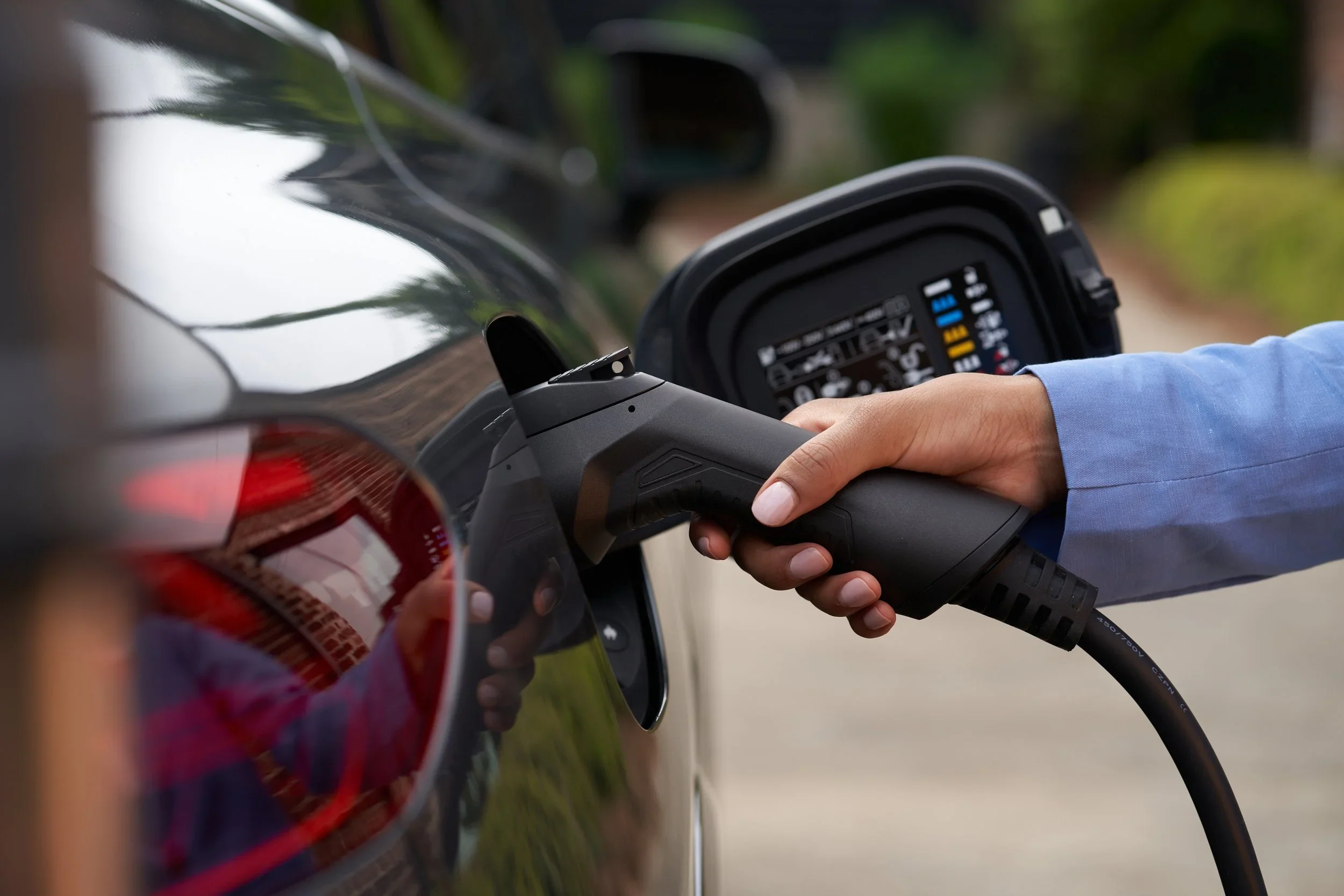 Person plugging in an electric car with a charging cable, focus on hand and vehicle's charging port.