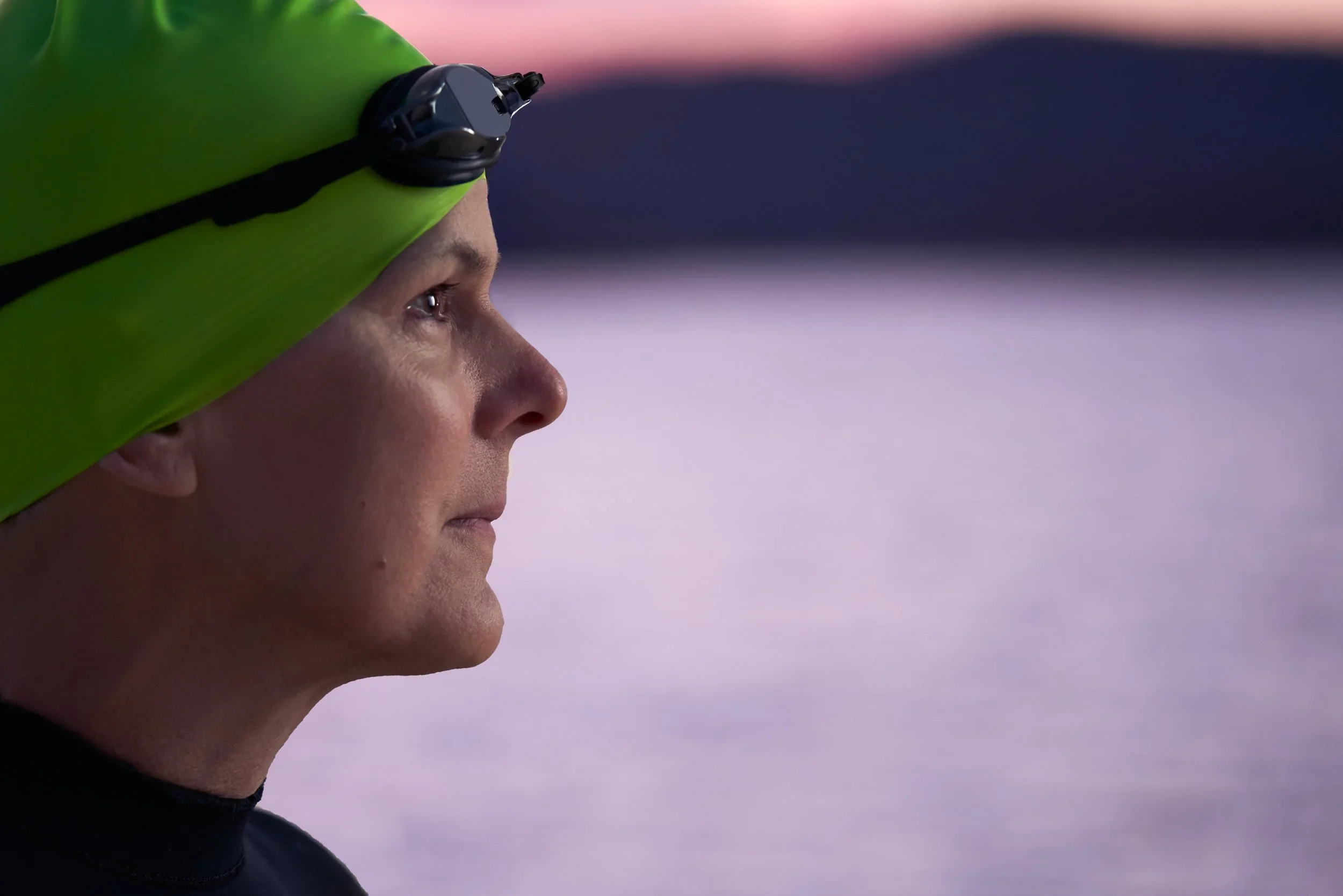Close-up side profile of a person wearing a green headband with a small black camera attached, standing outdoors at dusk with a blurred background.