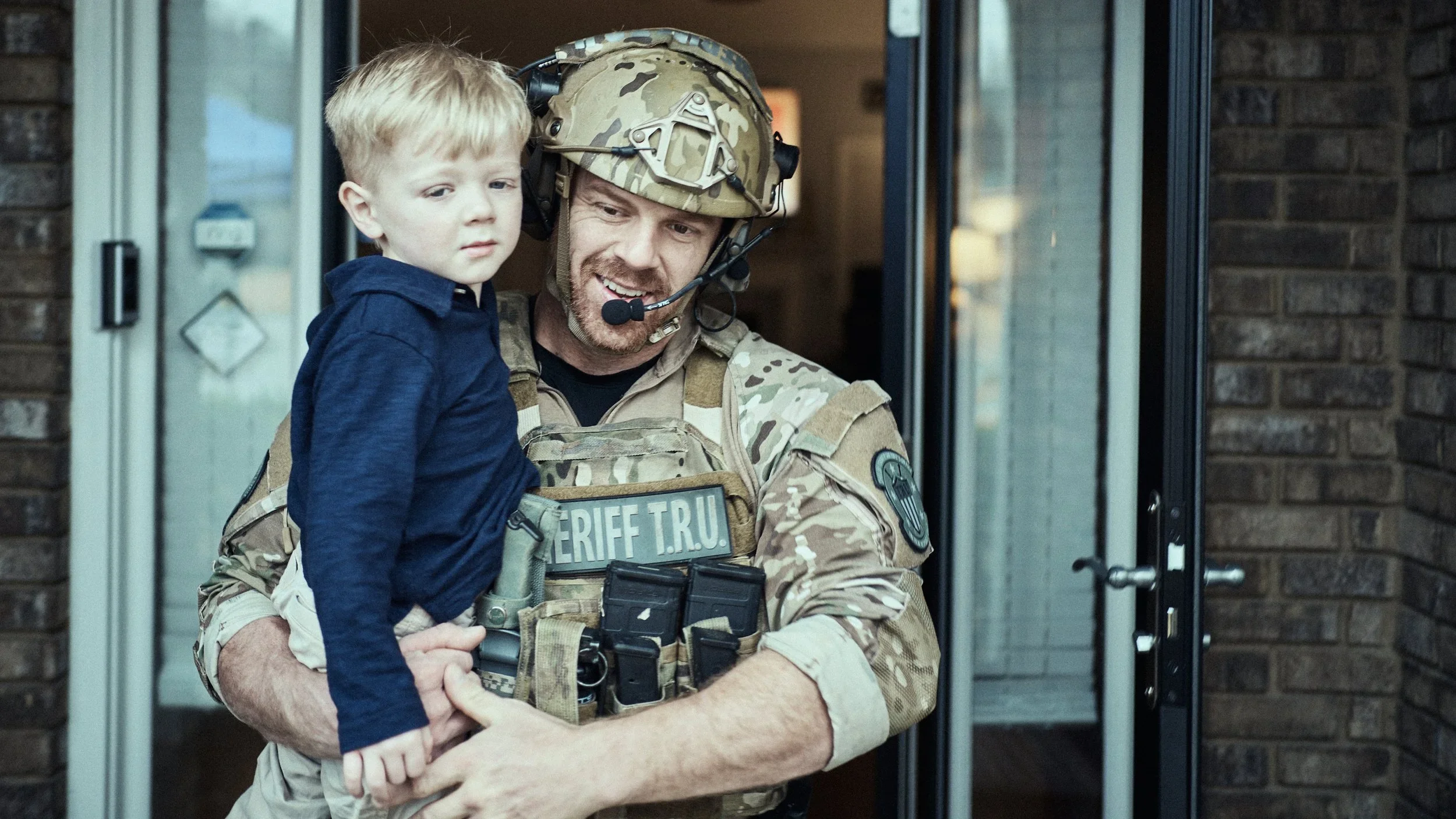 A Shelby County Sheriff’s Office tactical deputy holds a young boy near a brick building during a community event.