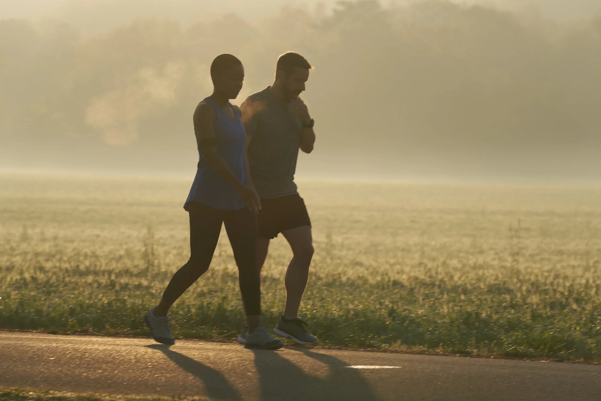 Two people jogging on a trail at sunset near a body of water, with mist in the background.