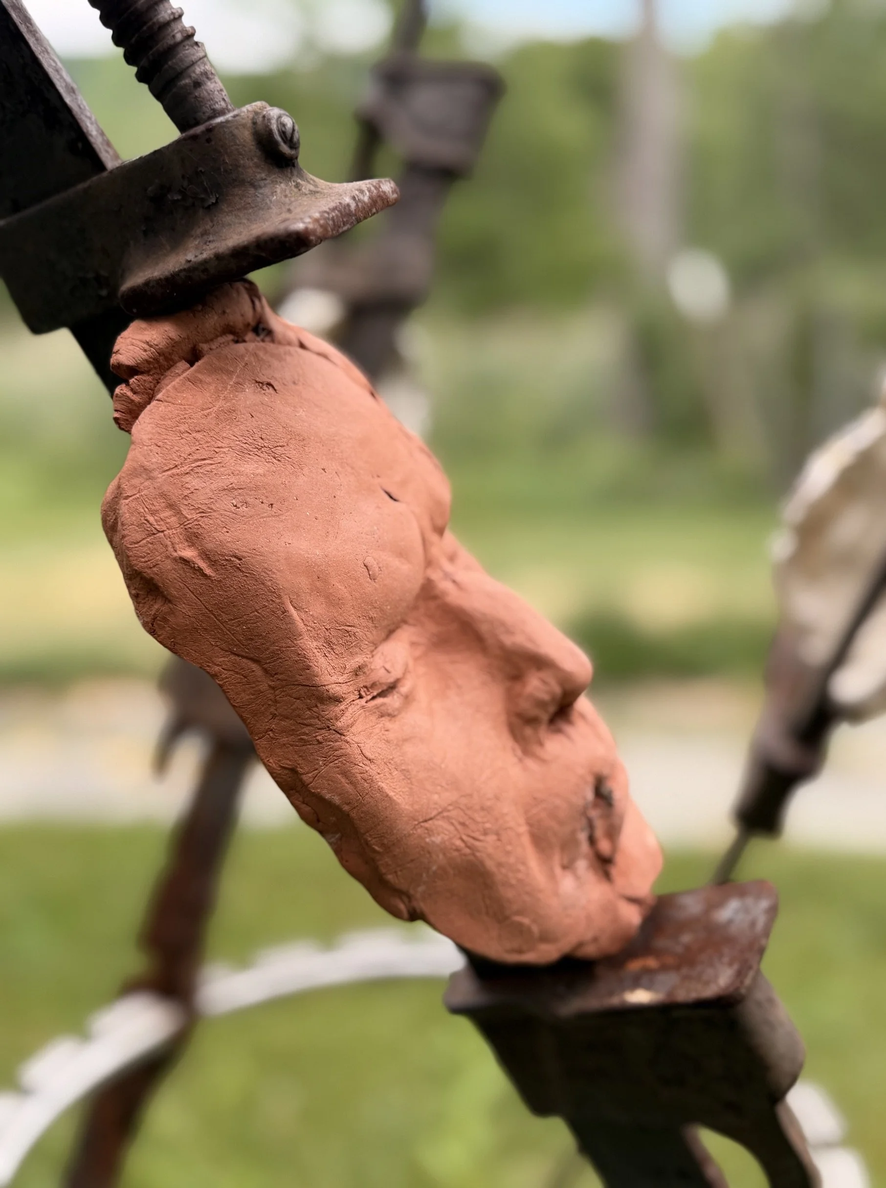 The Tribunal, outdoor sculpture by New York sculptor Aleksandra Scepanovic featuring reclaimed industrial steel and fired clay figures. Red clay face detail 