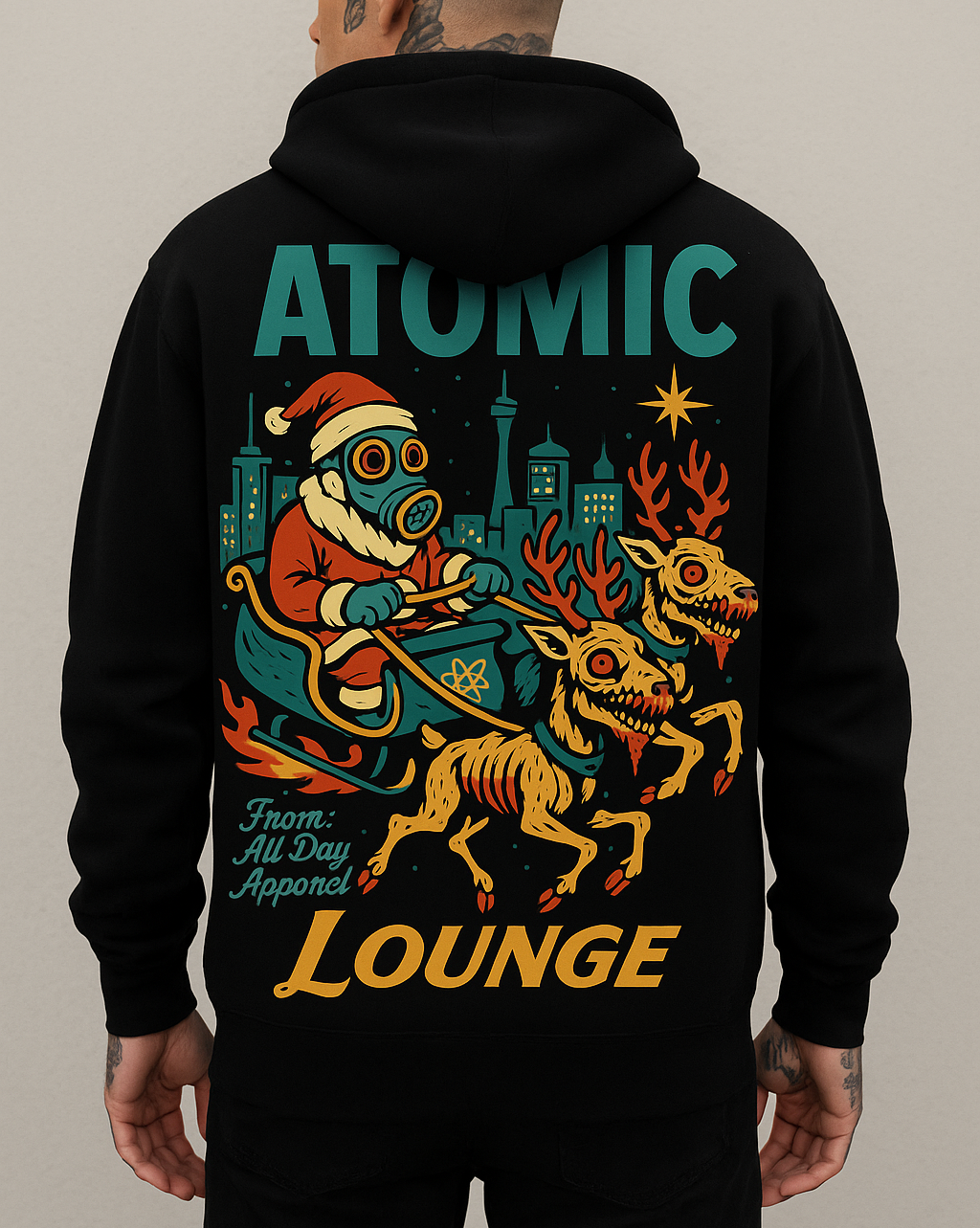 A person wearing a black hoodie with colorful graphic art on the back, depicting a robotic Santa riding a sleigh with two red-eyed, snarling dog-like creatures, with a cityscape in the background and the words 'Atomic Lounge' and 'From: All Day Apparel'.