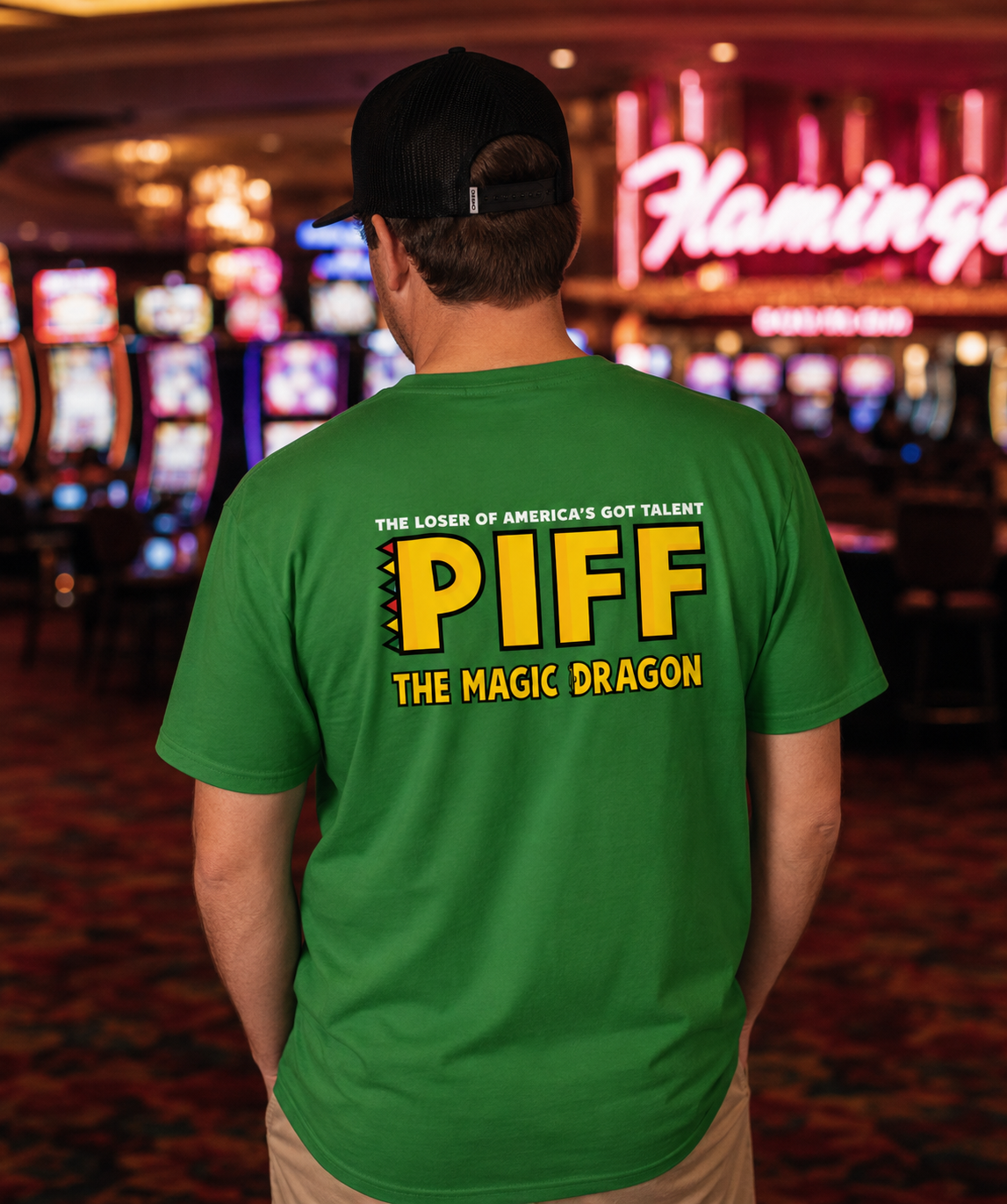 Man wearing a green T-shirt with the text 'The Loser of America's Got Talent Piff the Magic Dragon' on the back, standing in a casino with slot machines and neon signs in the background.