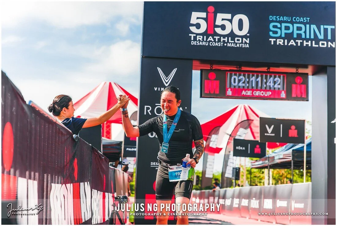 Triathlete celebrating with a high-five after crossing the finish line at the Desaru Coast Sprint Triathlon.