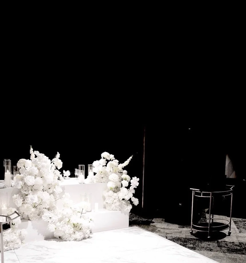 White floral arrangements and candles on a table, with a black background.