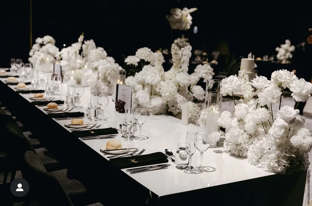 Elegant banquet table decorated with white flowers, candles, glassware, and black napkins for a formal event or wedding reception.